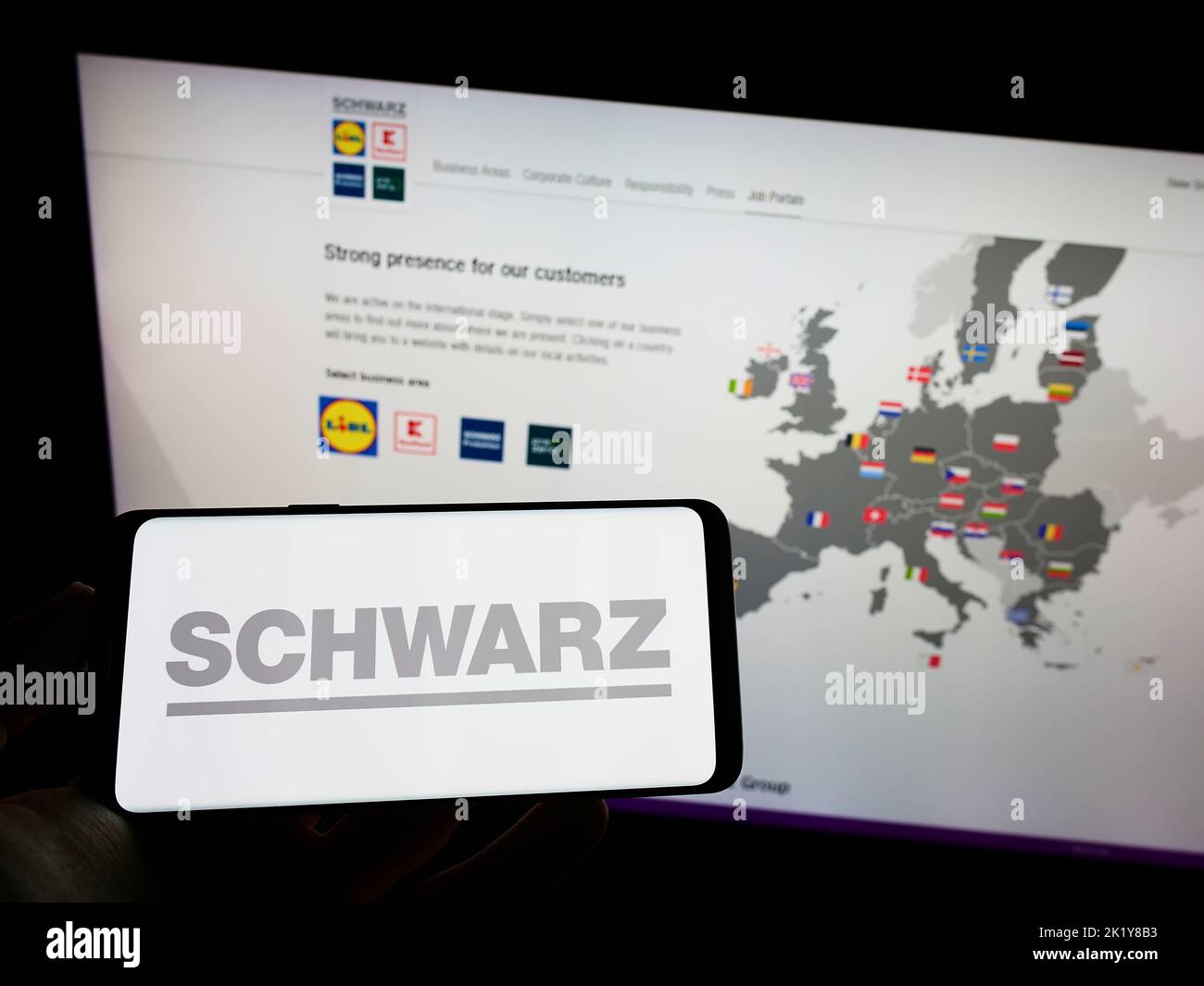 Persona che tiene il cellulare con il logo della società tedesca di vendita al dettaglio Schwarz Group sullo schermo di fronte al sito web aziendale. Messa a fuoco sul display del telefono. Foto Stock