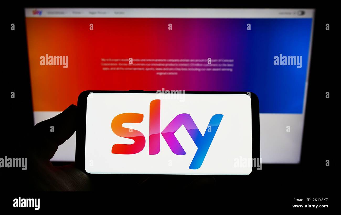 Persona che detiene uno smartphone con il logo della società di media britannica Sky Group Limited sullo schermo davanti al sito Web. Messa a fuoco sul display del telefono. Foto Stock