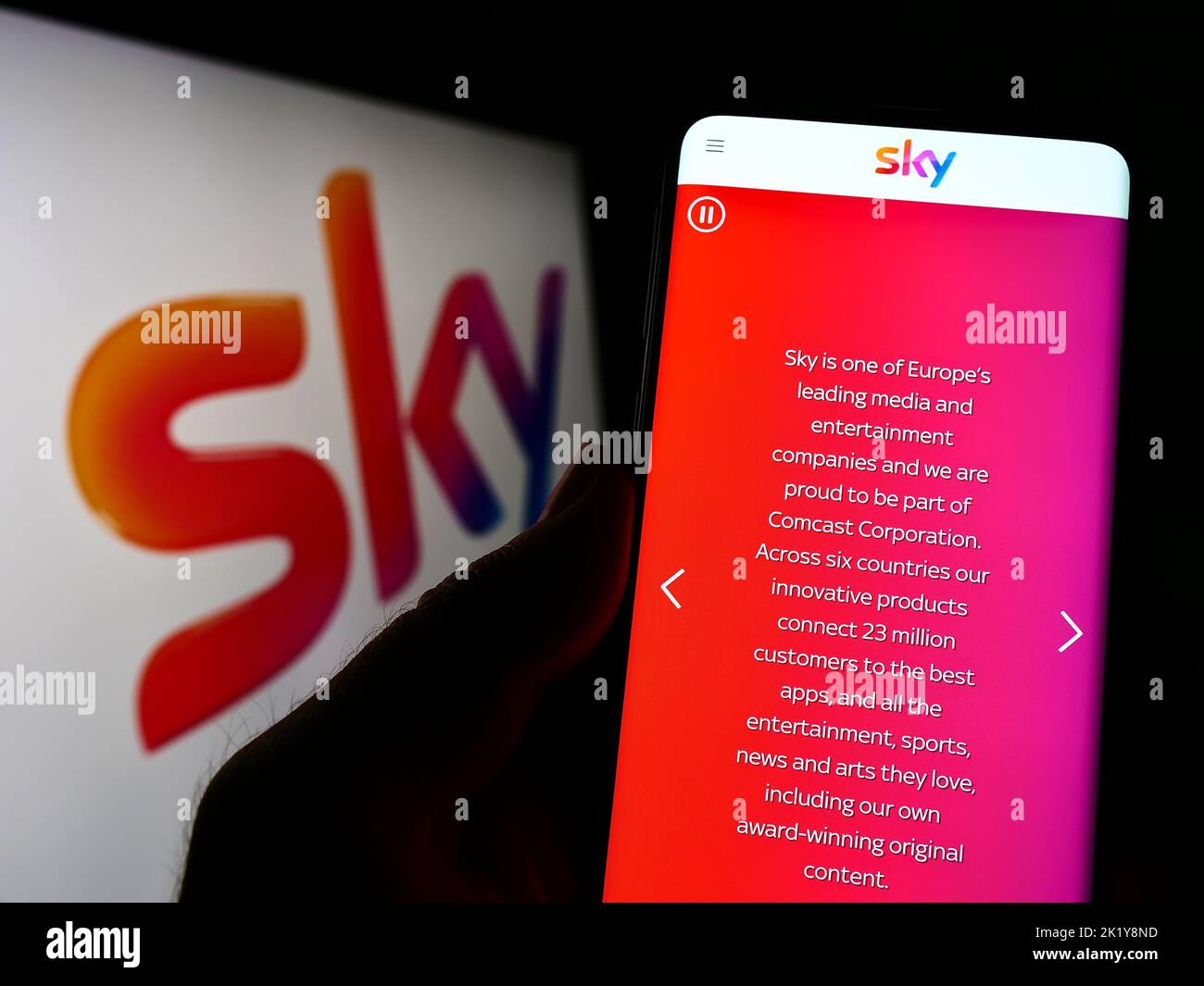 Persona che tiene uno smartphone con il sito Web della società di media britannica Sky Group Limited sullo schermo davanti al logo. Messa a fuoco al centro del display del telefono. Foto Stock
