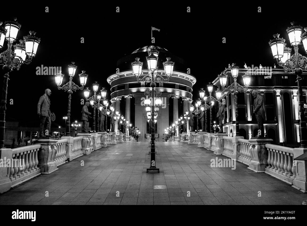Statue che decorano il Ponte dell'Arte, attraversando il fiume Vardar, Skopje, Macedonia settentrionale. Di notte con lampioni che illuminano il ponte. Foto Stock
