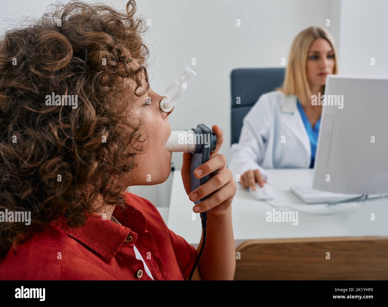 Bambino maschio durante il test di spirometria respiratoria e di funzionalità polmonare utilizzando spirometro medico con il medico che controlla i risultati del test sul monitor Foto Stock