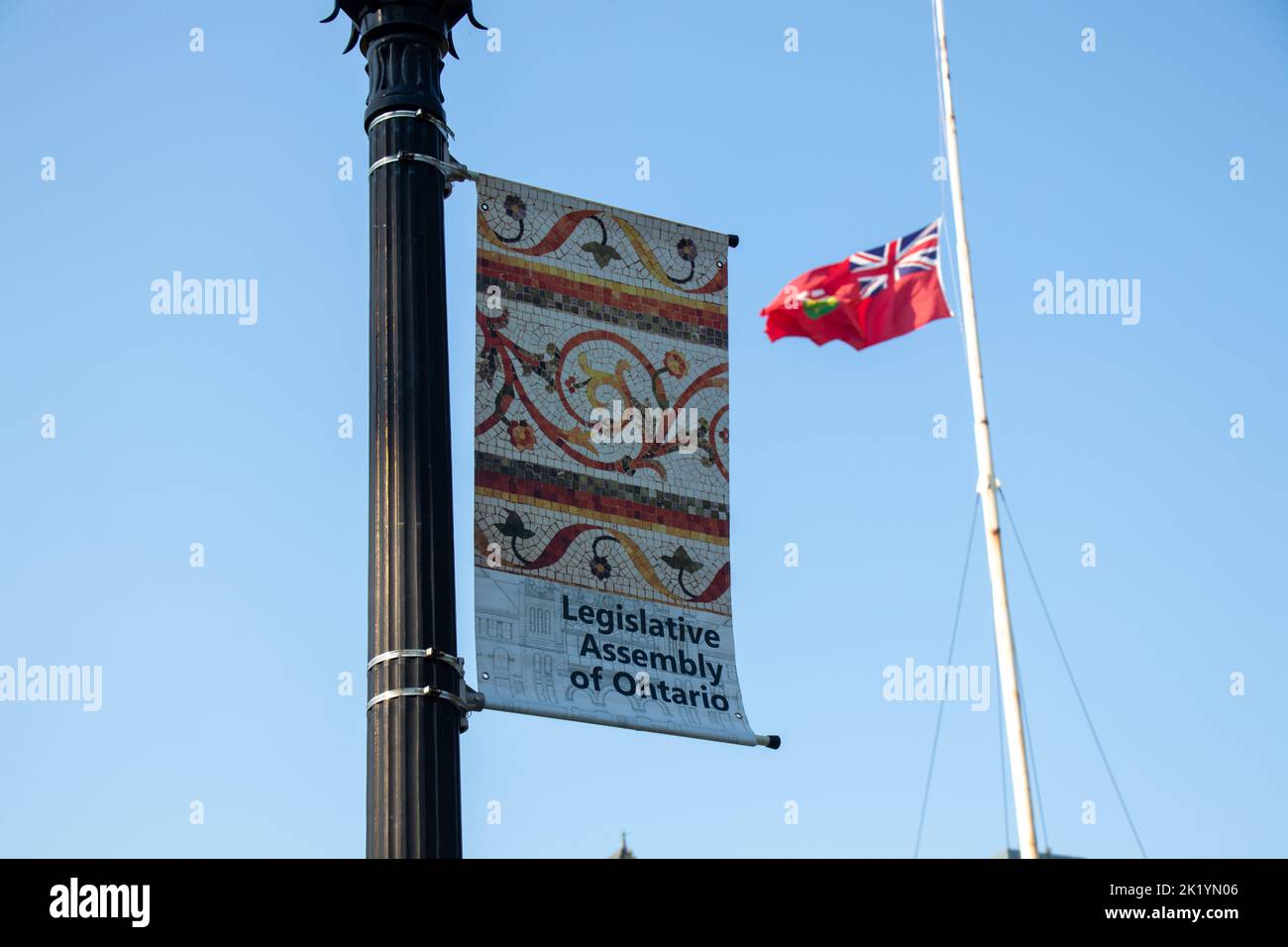Un banner per l'Assemblea legislativa dell'Ontario è visto su un post al Queens Park con la bandiera dell'Ontario che sventola sullo sfondo. Foto Stock