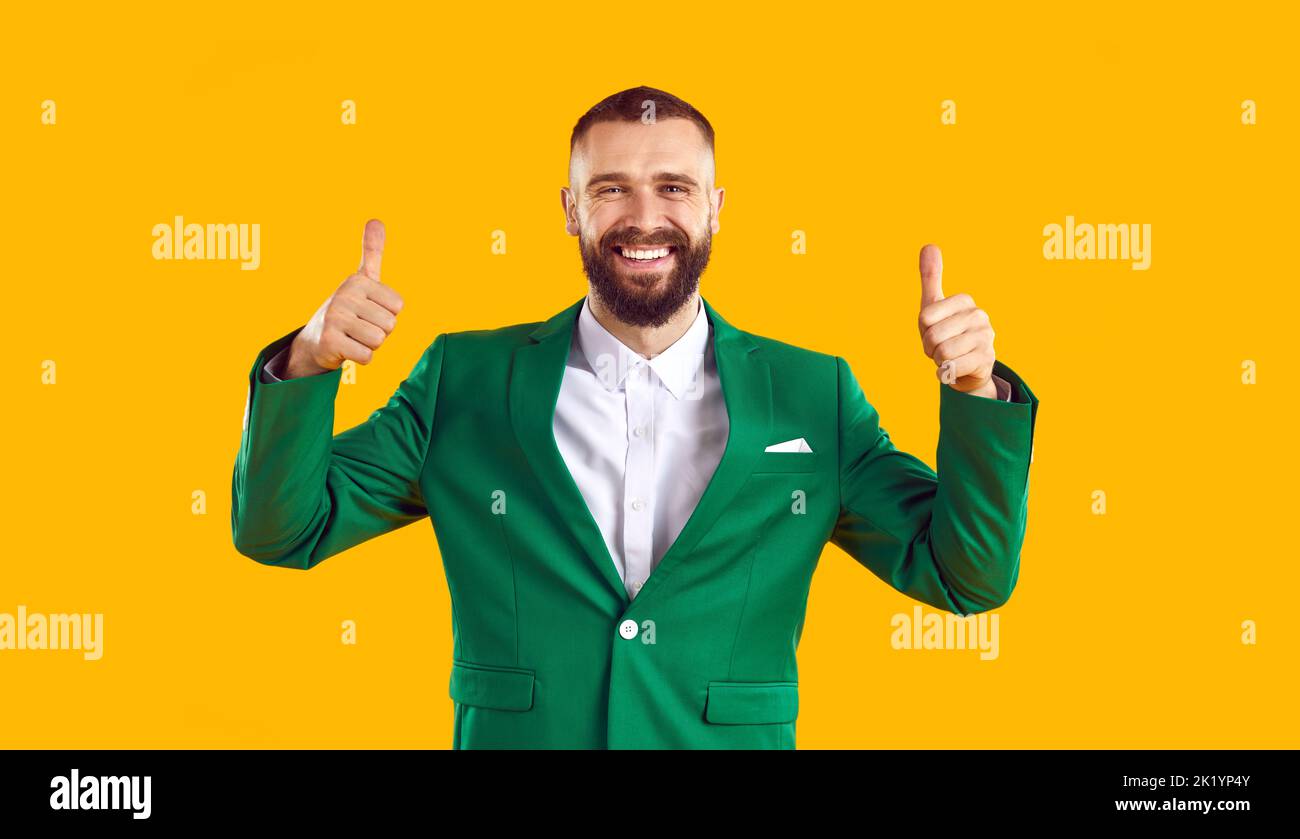 Felice uomo in vestito verde sorridente e mostrando pollici isolato su sfondo giallo Foto Stock