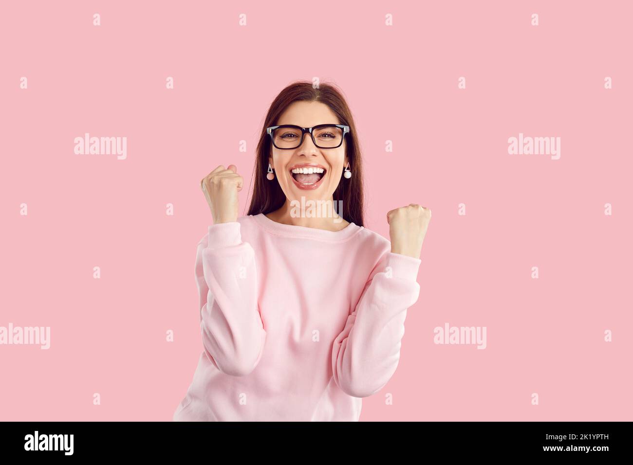 Felice donna eccitata gioisce il successo, pugni aggrappati e esclama trionfalmente su sfondo rosa. Foto Stock
