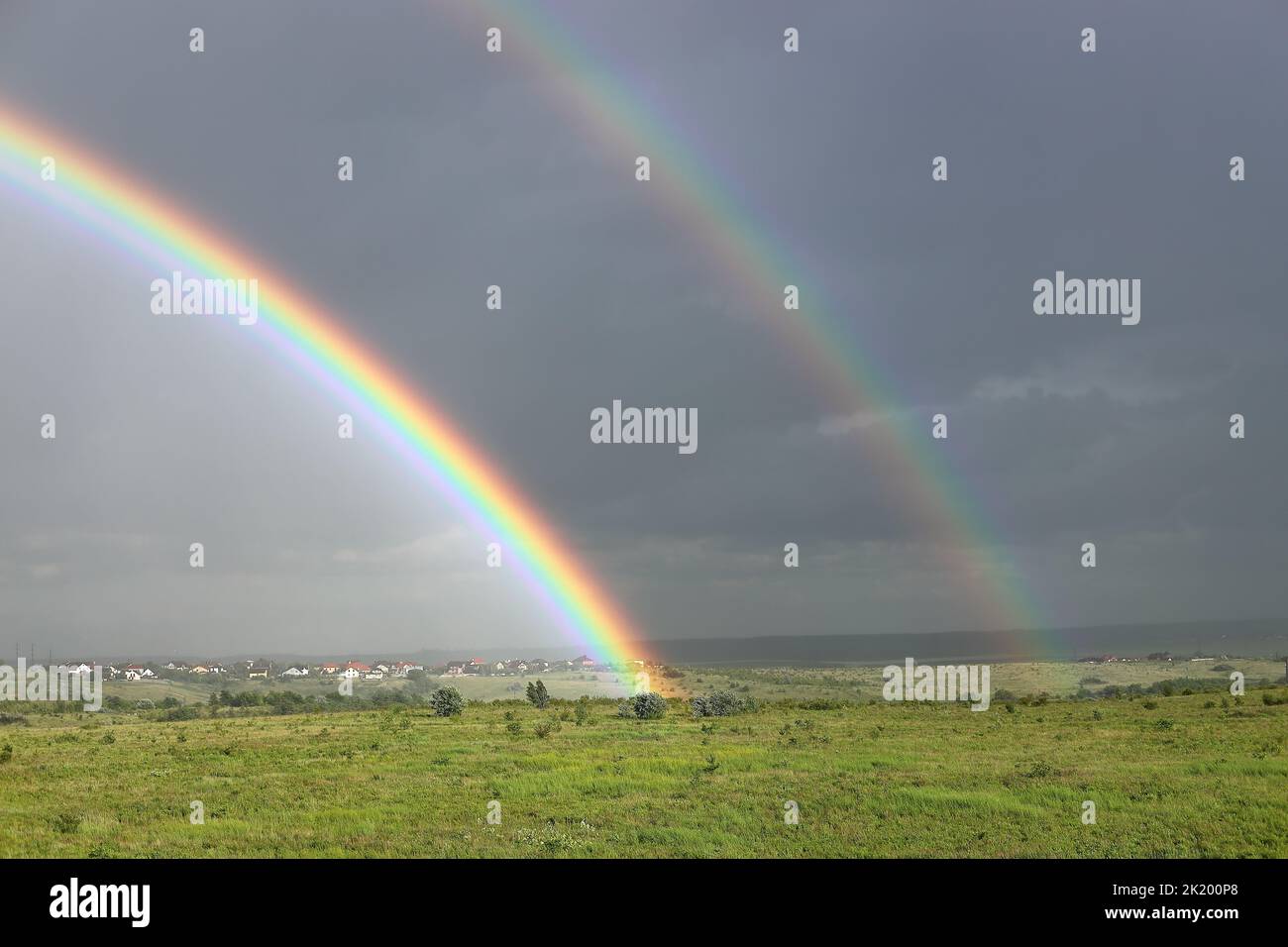 Doppio arcobaleno luminoso con nuvole di pioggia scure sullo sfondo Foto Stock