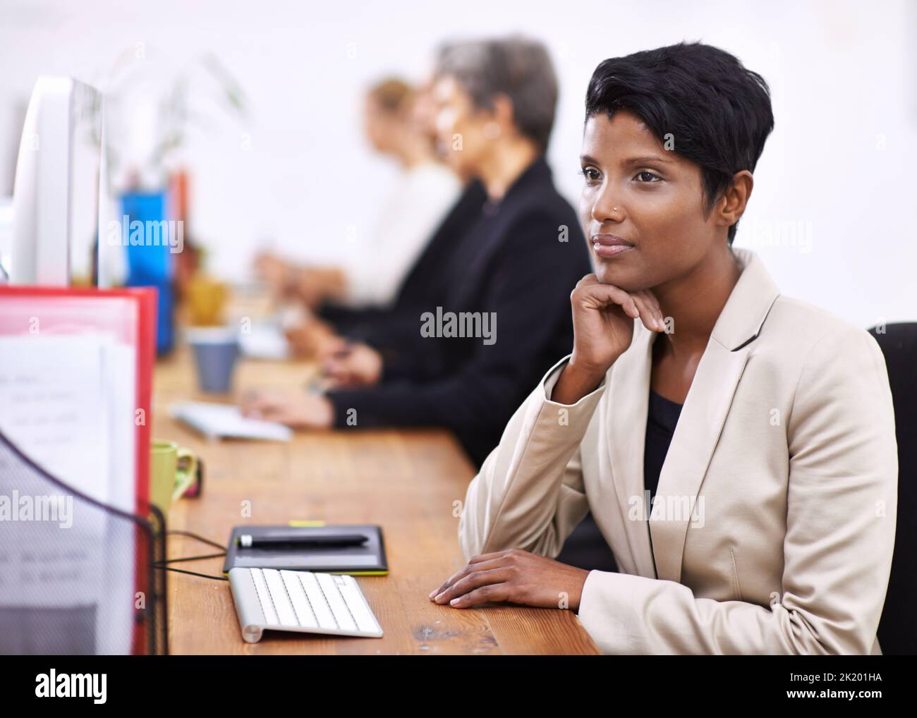 Una donna attraente seduta su una scrivania mentre si guarda distratta. Foto Stock