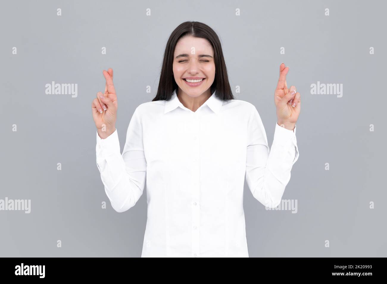 Ritratto di donna divertente con le dita incrociate per buona fortuna, sfondo isolato. Il colpo di testa della donna felice incrocia le dita con espressione positiva Foto Stock