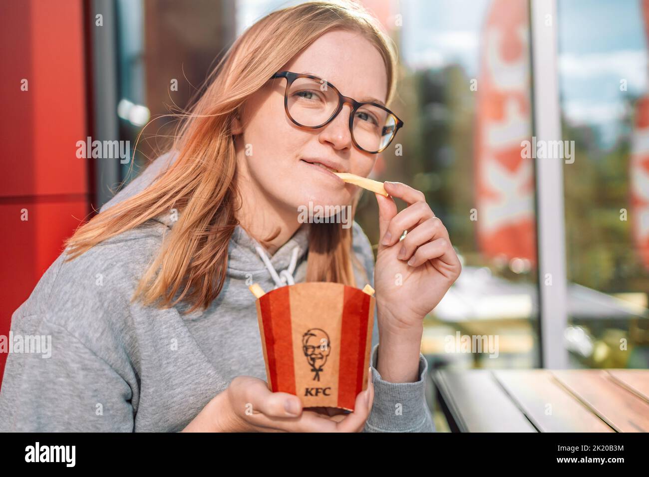 Fast food KFC. Cracovia, Polonia - Settembre 11 2022: Una bella donna bionda sta gustando patatine fritte in un ristorante KFC. Nessuna dieta. Foto Stock