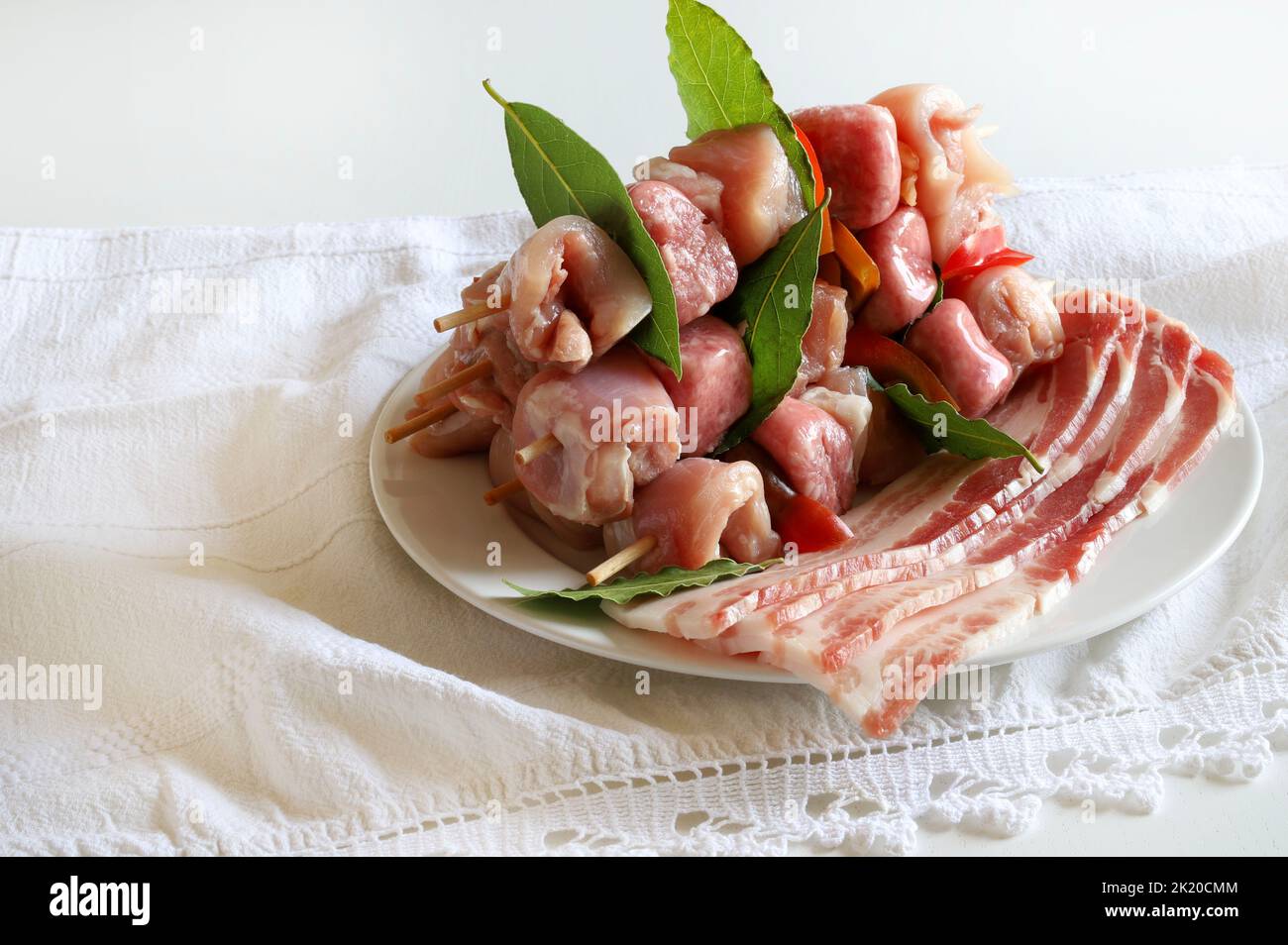 Spiedini con carne cruda e pancetta isolati su fondo bianco. Foto Stock