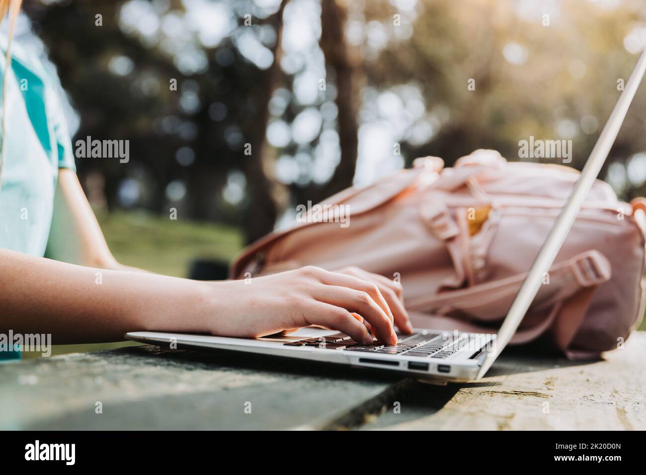 Studentessa universitaria irriconoscibile che utilizza il suo computer portatile nel parco naturale del campus. T-shirt turchese e zaino rosa. Foto Stock