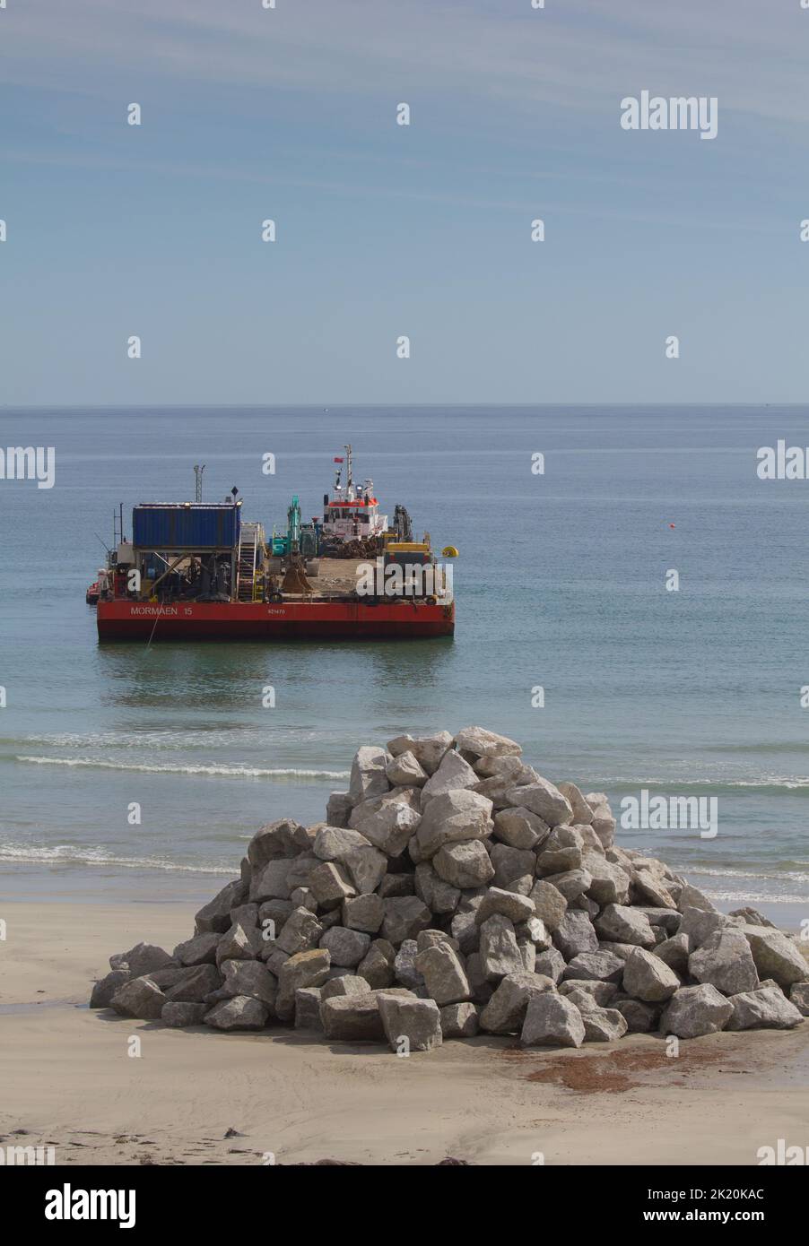 Rocce di armatura scaricate per la costruzione di frangiflutti Coverack Bay con chiatta di trasporto. Foto Stock