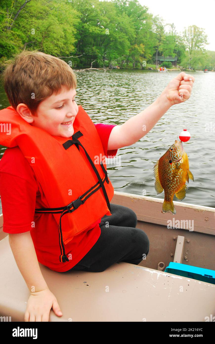 Un giovane ragazzo mostra con orgoglio il primo pesce che ha pescato mentre pesca su una barca su un lago Foto Stock