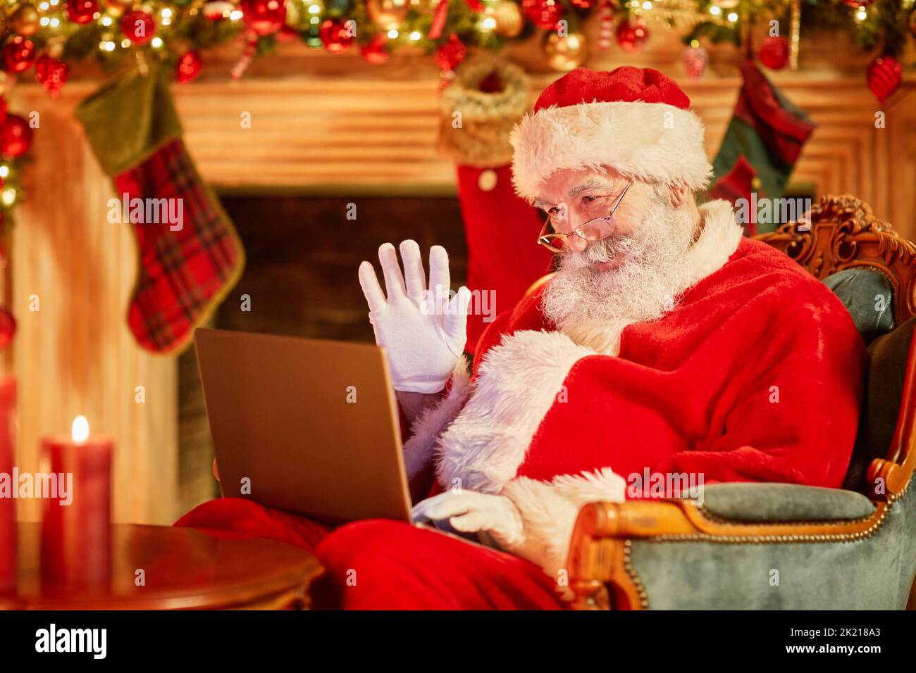 Ritratto di Babbo Natale tradizionale che ondula alla fotocamera in video chat mentre si utilizza il portatile dal caminetto Foto Stock