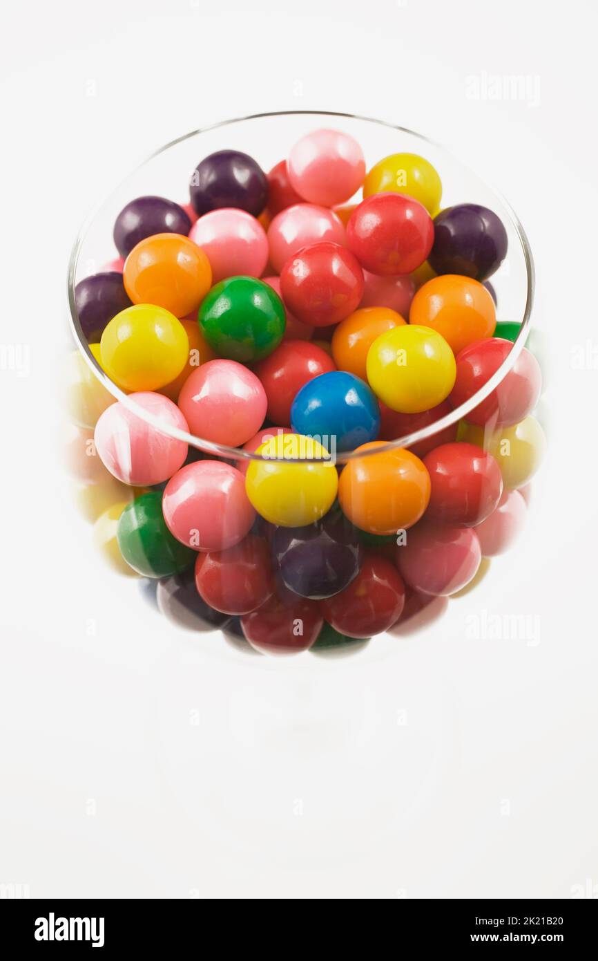 Polpette di gomma colorate assortite in bicchiere di vino su sfondo bianco. Foto Stock