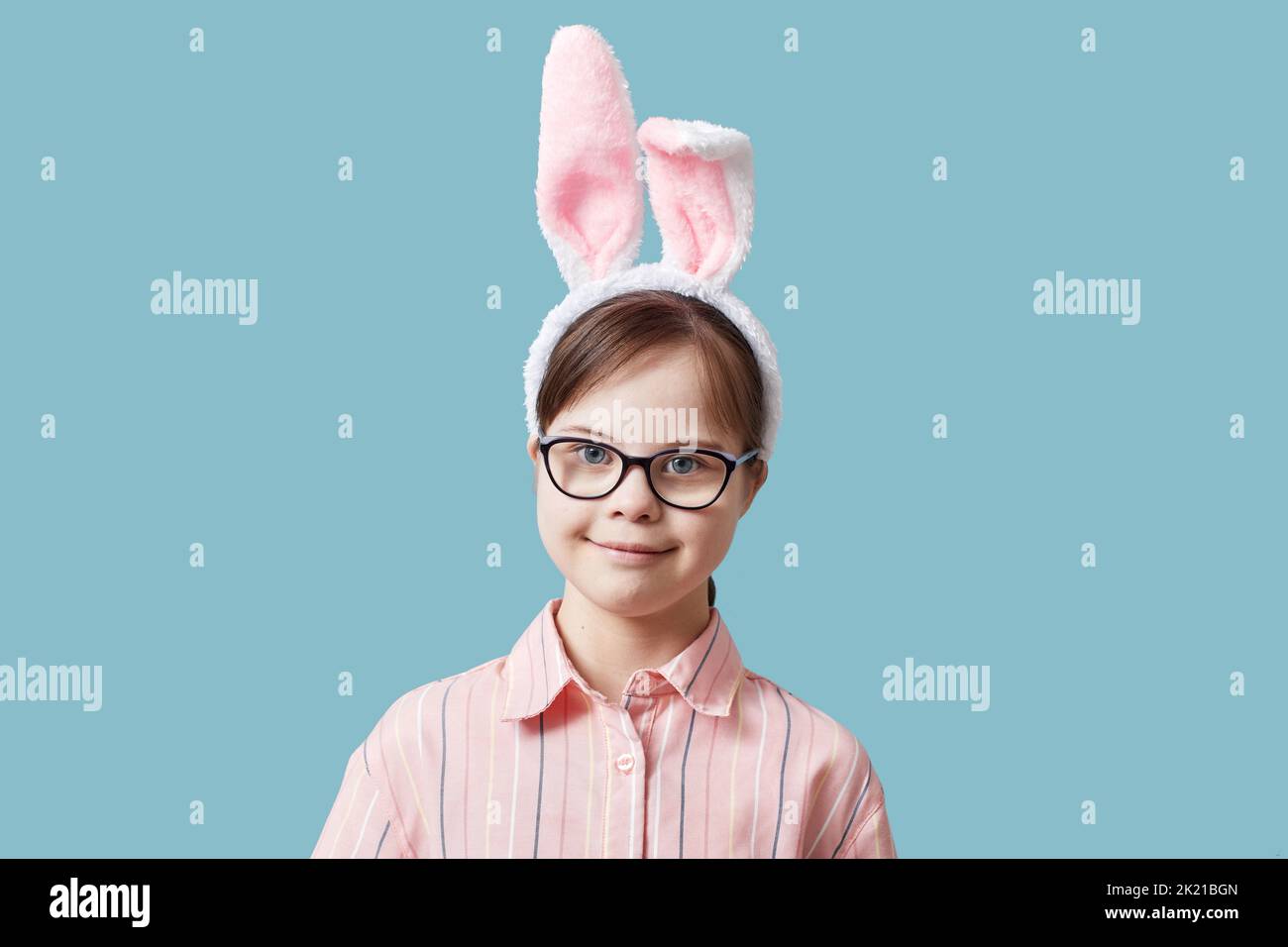 Ritratto di ragazza carina con sindrome di Down indossare coniglietto di Pasqua orecchie su sfondo blu Foto Stock