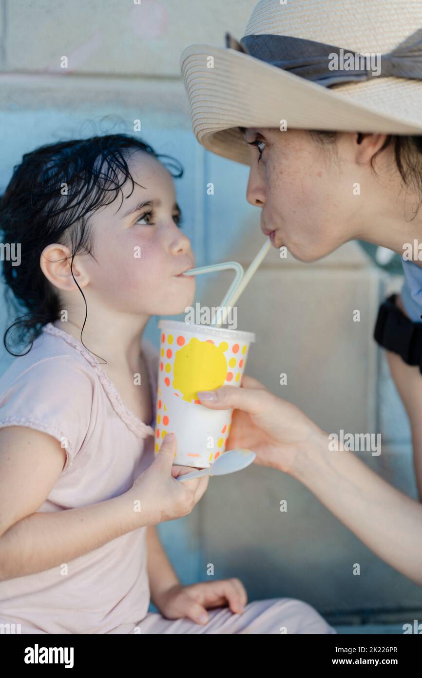 Madre e figlia bevono dalla stessa tazza con cannucce Foto Stock