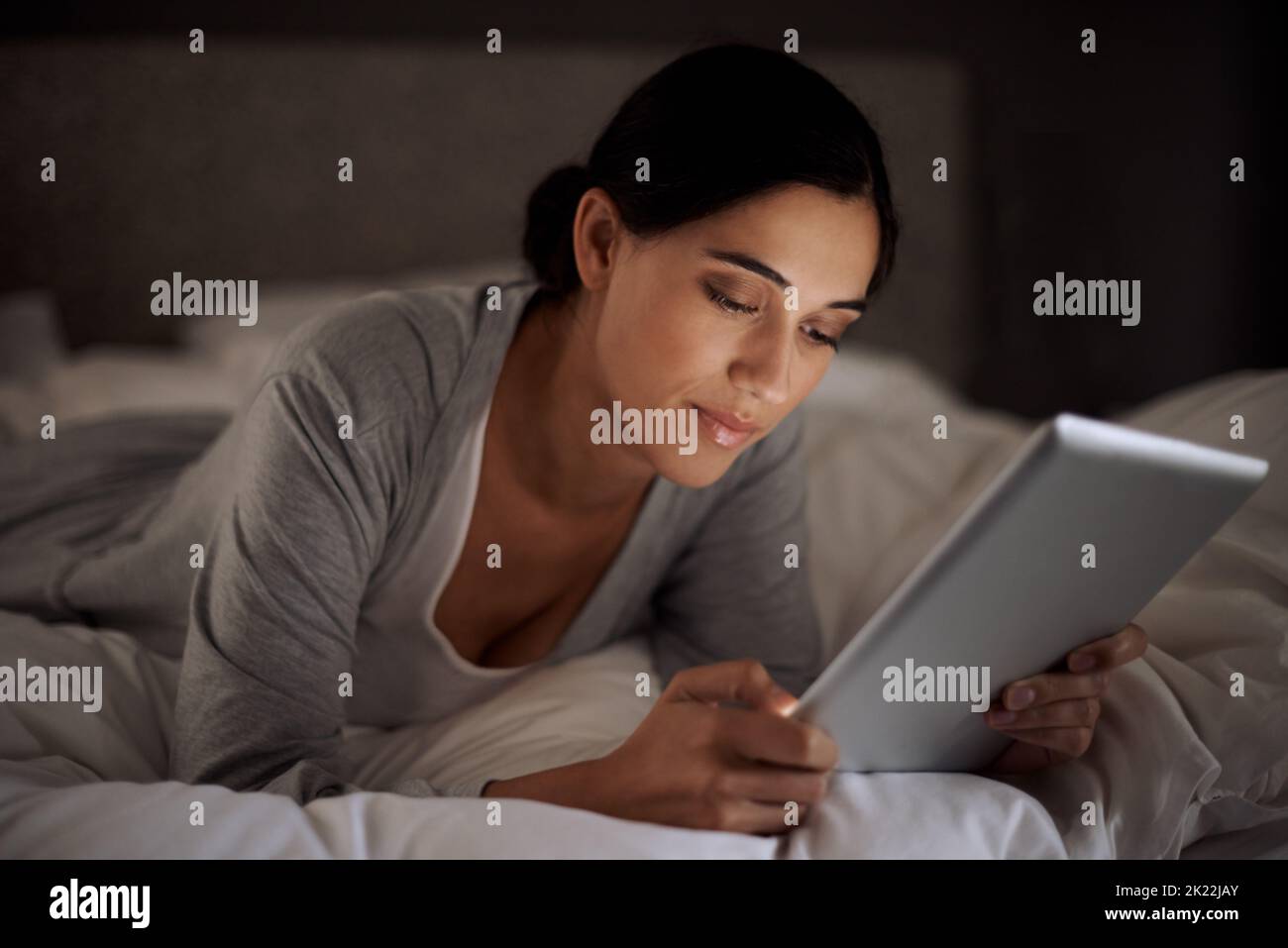 Prima di andare a letto, una giovane donna attraente che usa il suo tablet a letto. Foto Stock