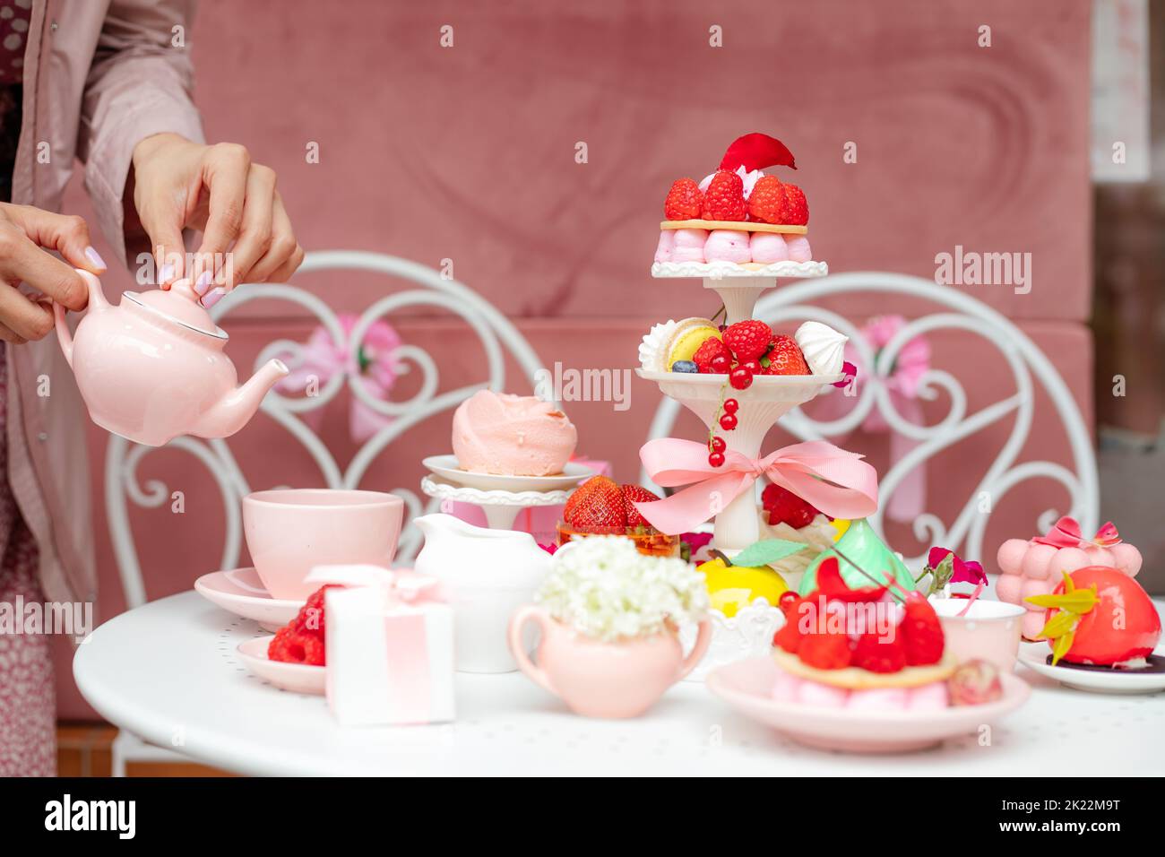 Serve un tavolo festoso con torte appetitose, dolci dolci, fragole fresche e lamponi, una persona può versare il tè nelle tazze del caffè. Festa in stile rosa Foto Stock