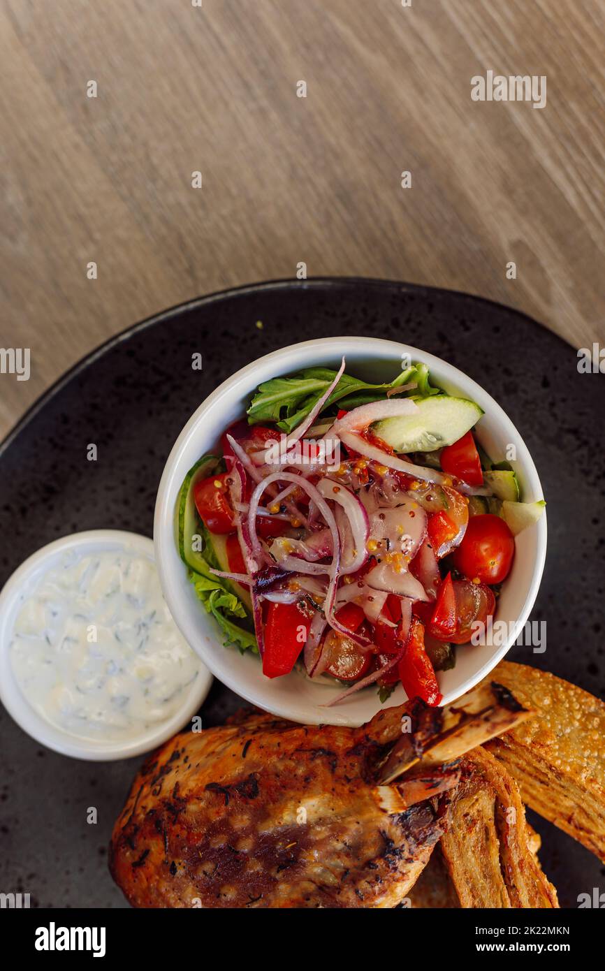 Pollo arrosto o anatra in verticale delizioso e succoso con insalata di verdure di cetrioli, pomodoro, cipolla, panini dolci sul tavolo Foto Stock