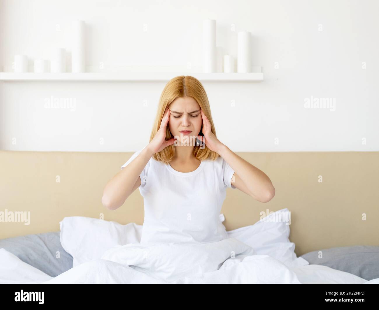 Mal di testa in camera. Disturbo da insonnia. Mancanza di sonno. Problema di salute. Donna infelice sofferente a letto con coperta bianca che tocca templi in migrai Foto Stock