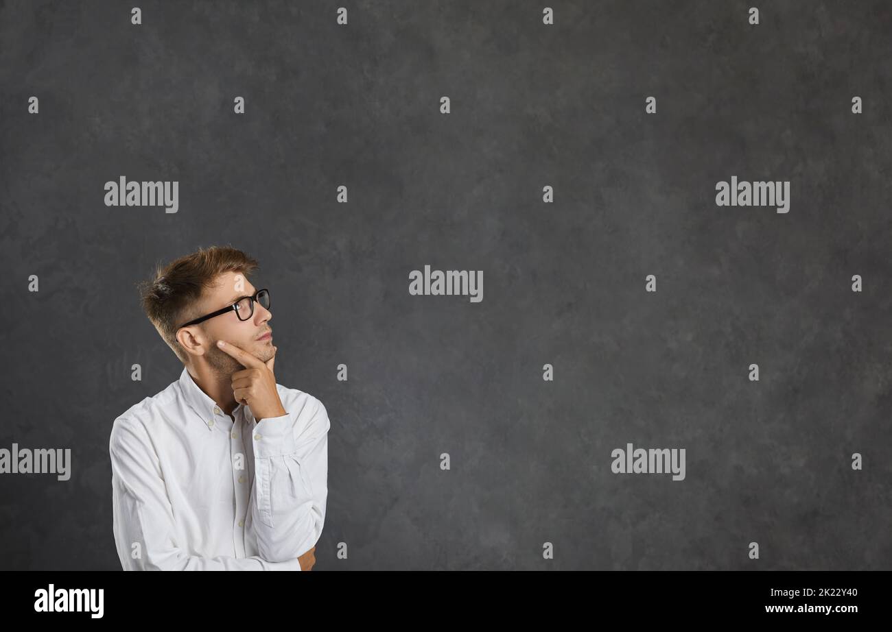 Giovane pensatore maschile sognante guarda penosamente lo spazio libero per il testo su sfondo grigio. Foto Stock