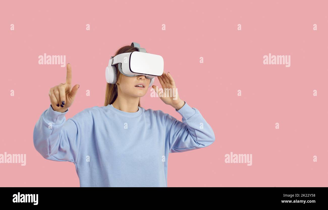 Giovane donna su sfondo rosa che vive la realtà virtuale utilizzando moderni occhiali VR Foto Stock