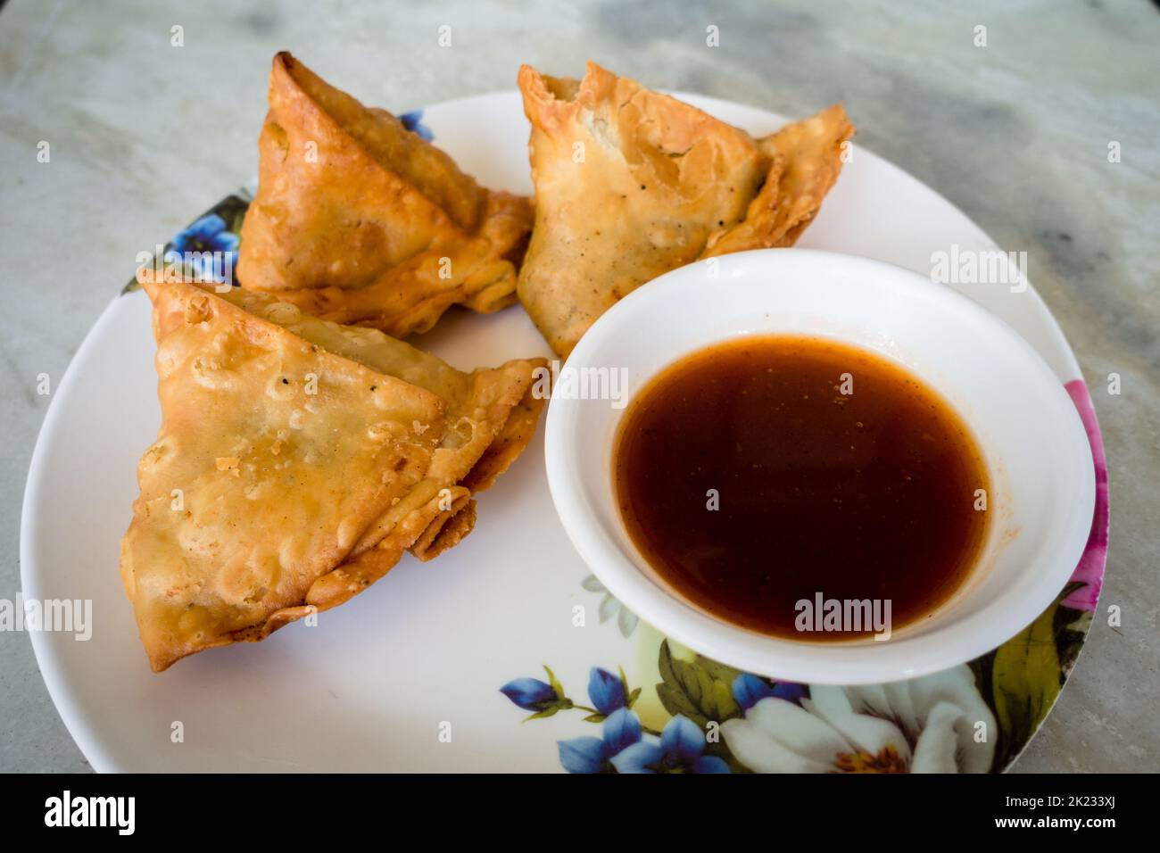 Samosa con salsa di tamarindo o chutney. Una samosa o singara è una pasta fritta o al forno con un ripieno salato, compresi ingredienti come la pota speziata Foto Stock