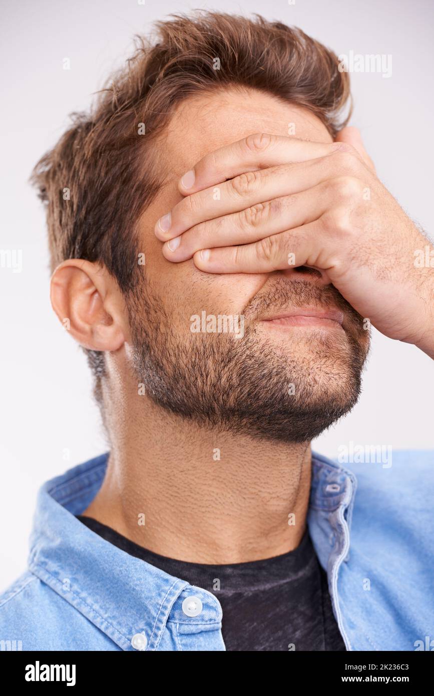 Facepalm. Studio shot di un bel giovane che copre gli occhi con rammarico contro uno sfondo grigio. Foto Stock