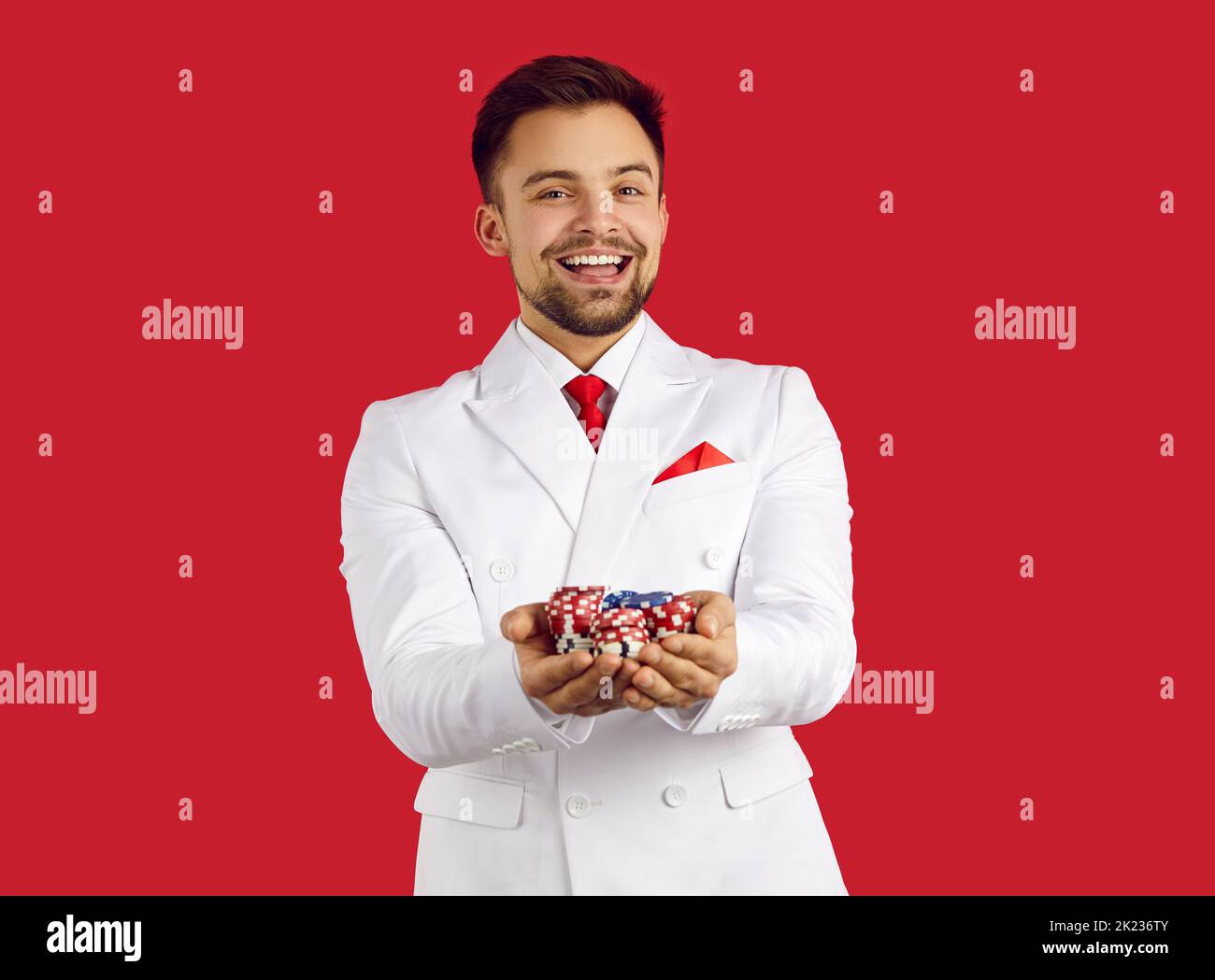 Ritratto di uomo felice che tiene chip di poker nelle sue mani isolato su sfondo rosso. Foto Stock