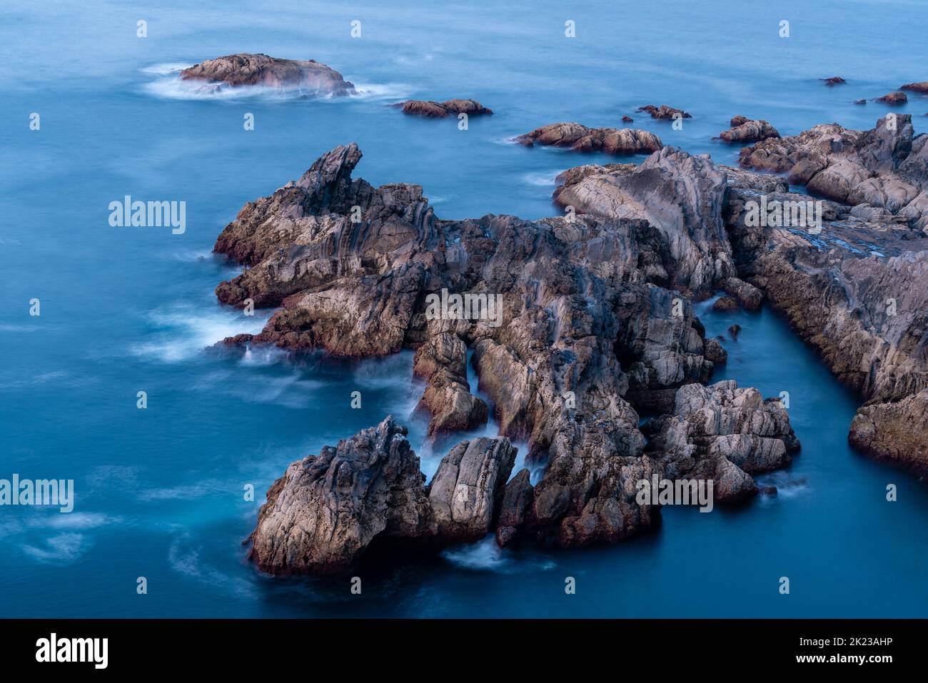 Lunga esposizione di mare e rocce. Onde che spruzzano sulla roccia creando una bella foto. Splendidi colori al tramonto. Paesaggio delle Asturie Foto Stock