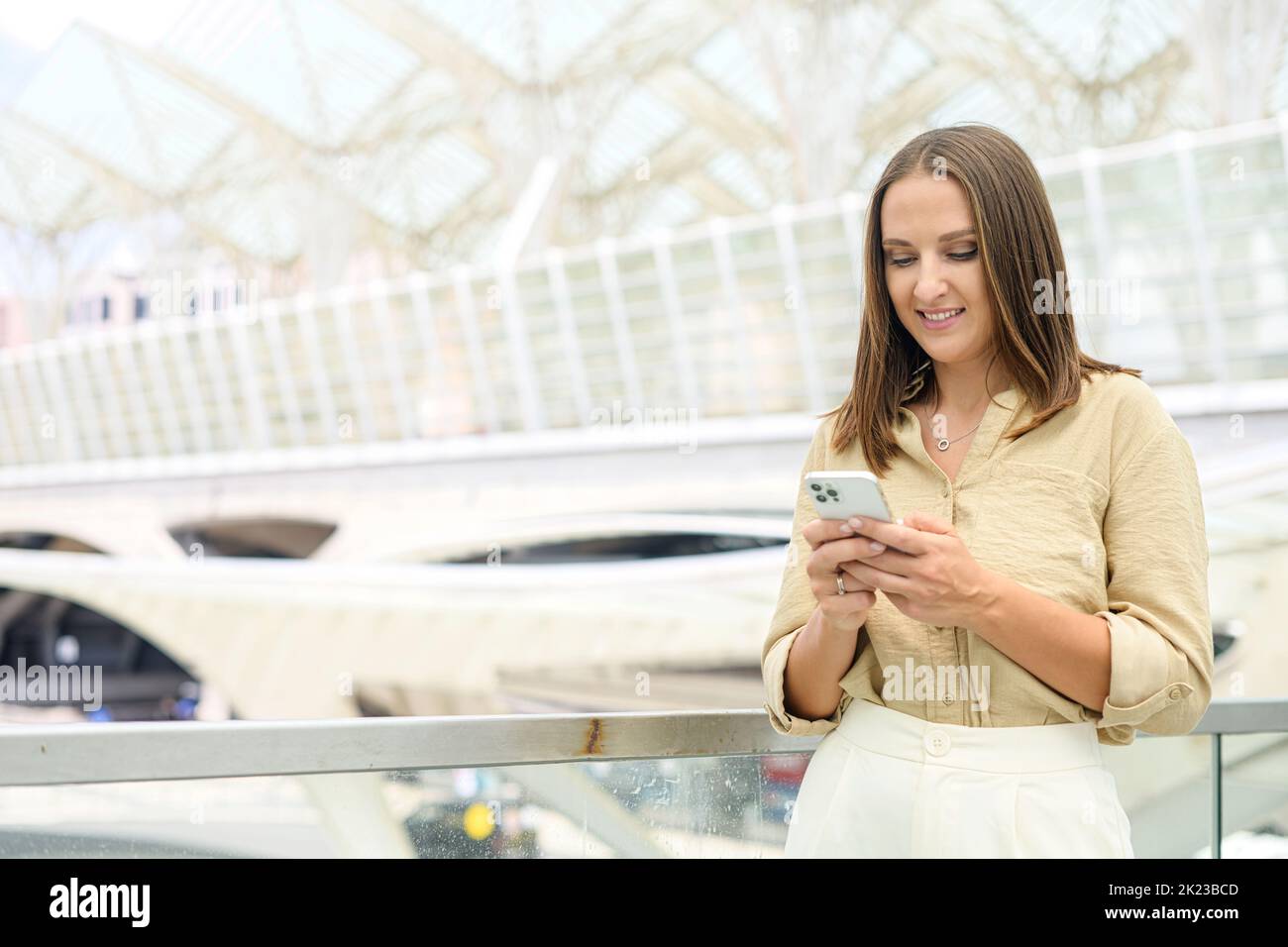 Il vestito giovane donna si trova sulla strada della città in centro e utilizza lo smartphone. Spensierate l'impiegato dell'ufficio femminile usando il cellulare sulla strada della città con il background urbano, gode di chating in linea Foto Stock