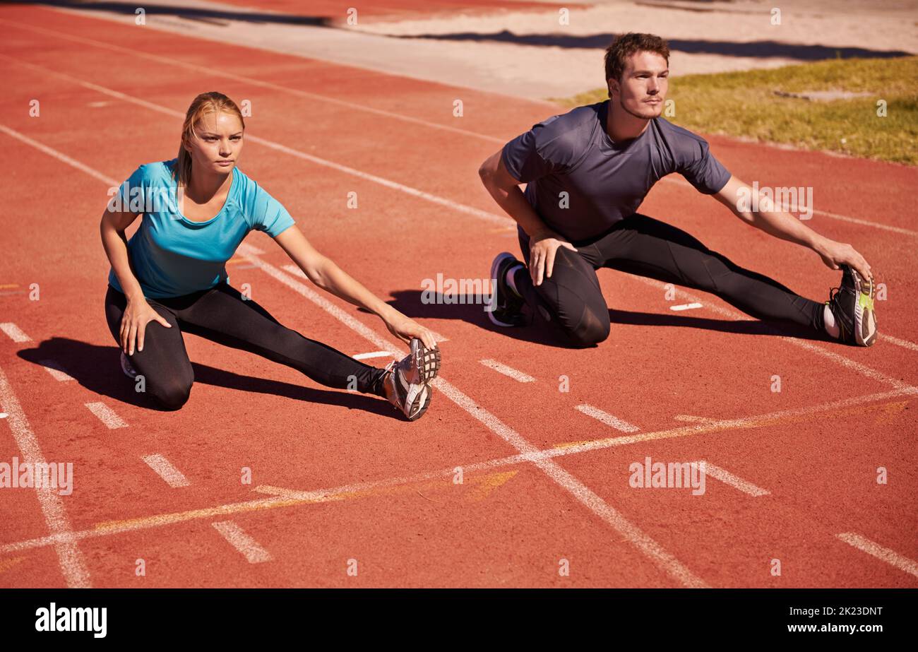 Scaldarsi per portarti giù. Due giovani che si allungano su una pista da atletica. Foto Stock