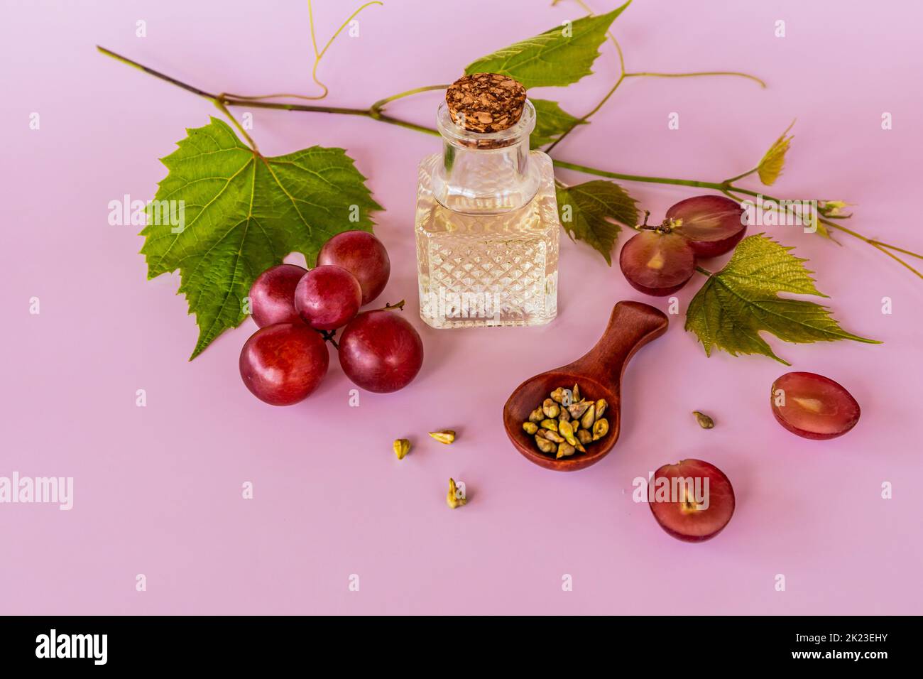 olio di semi d'uva in una bottiglia di vetro trasparente con tappo su fondo rosa e vite. alto contenuto di vitamine, minerali Foto Stock