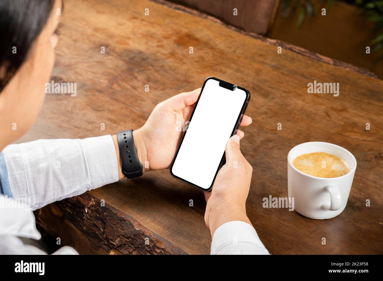 Verticale per smartphone, vista dalla spalla per smartphone verticale. Donna che usa un notebook moderno su un tavolo di legno. Bere caffè caldo fresco Foto Stock