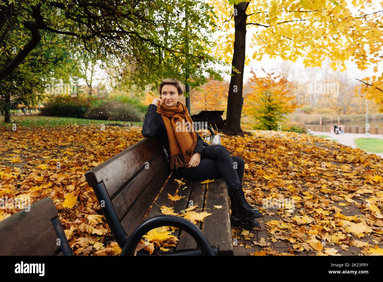 La bionda dai capelli corti riposa in un parco autunnale seduto su una panca Foto Stock