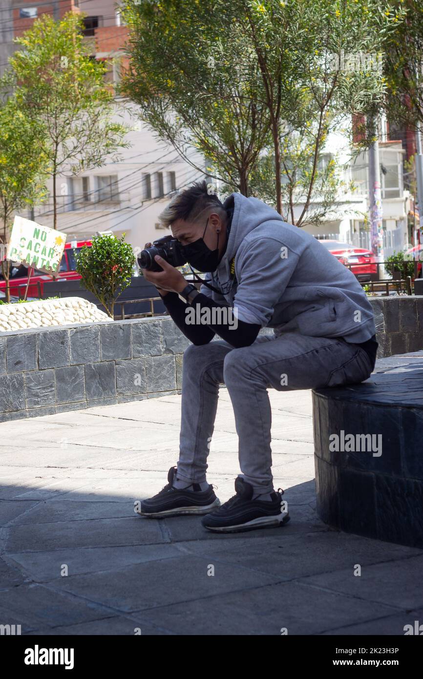 La Paz, Bolivia - Settembre 11 2022: Giovane uomo boliviano con un'acconciatura moderna è vestito in Gray sta scattando una foto nella piazza principale di Miraflore Foto Stock