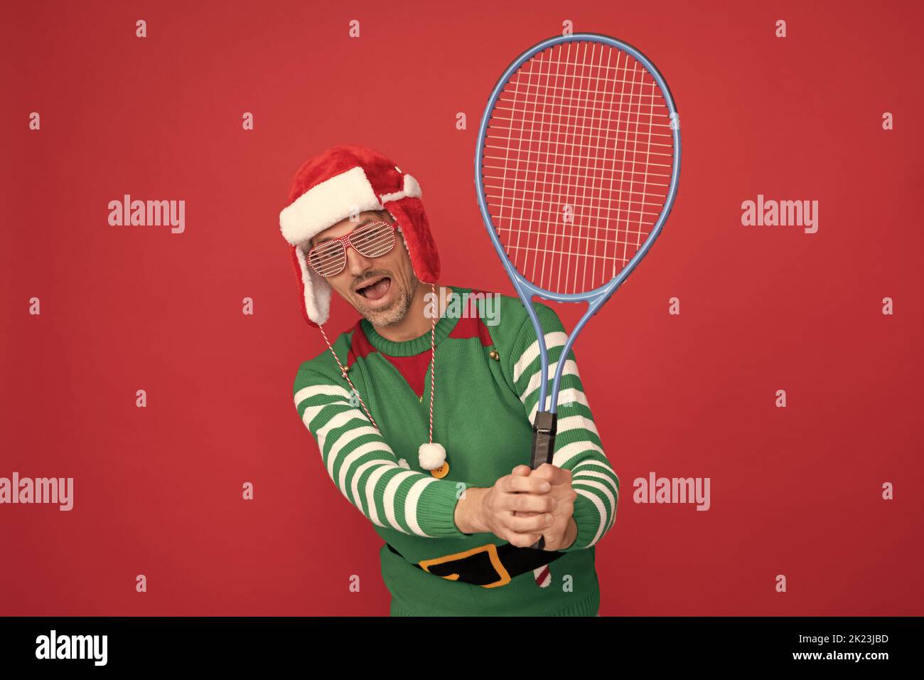 uomo stupito in costume di elfo e cappello di babbo natale. ragazzo di natale tenere il razzo da tennis Foto Stock