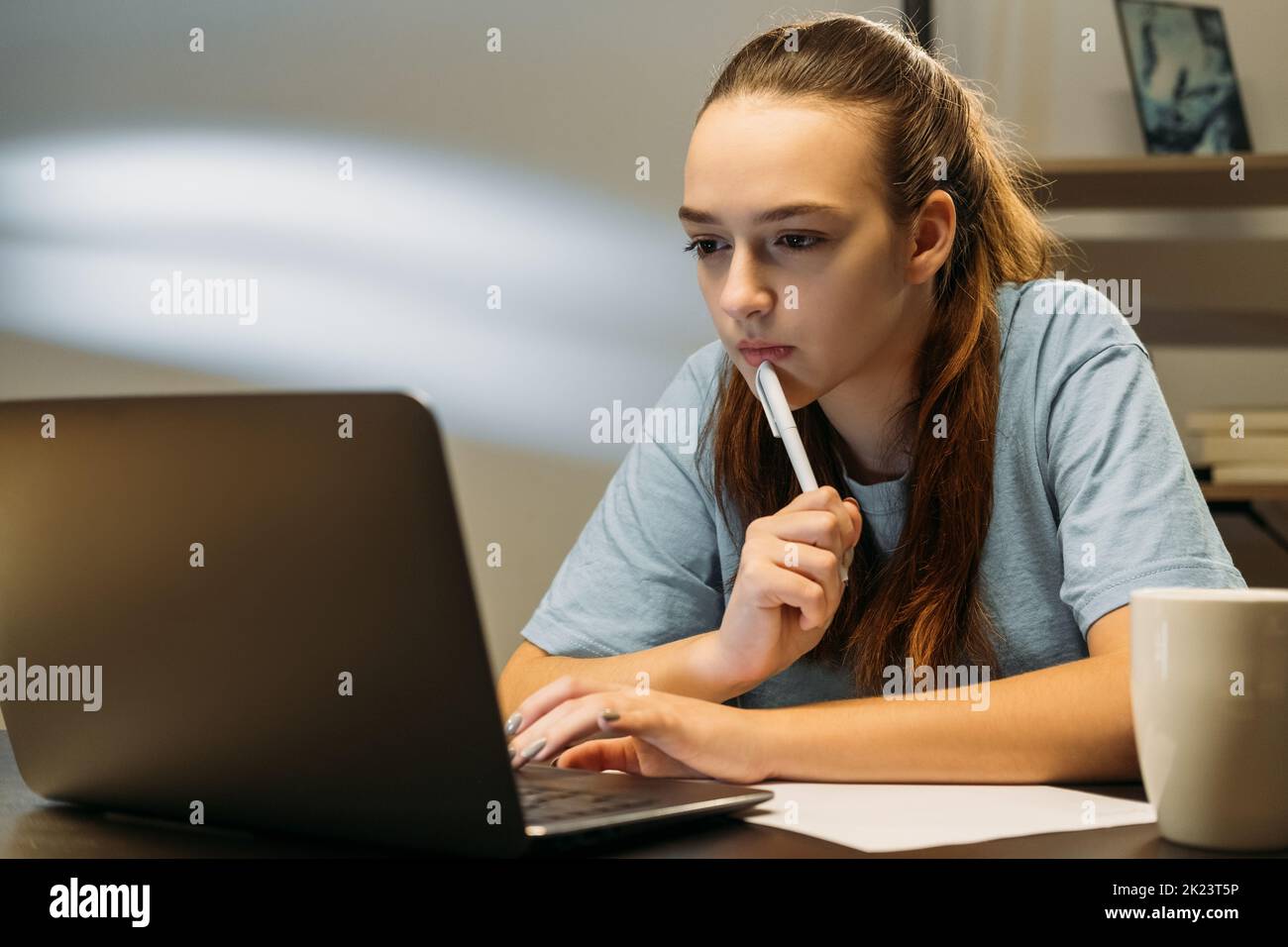 Autoeducazione. Apprendimento a distanza. Stile di vita di blocco Pandemia. Ragazza studentesca che scrive le note dal portatile seduto alla scrivania a tarda notte Foto Stock