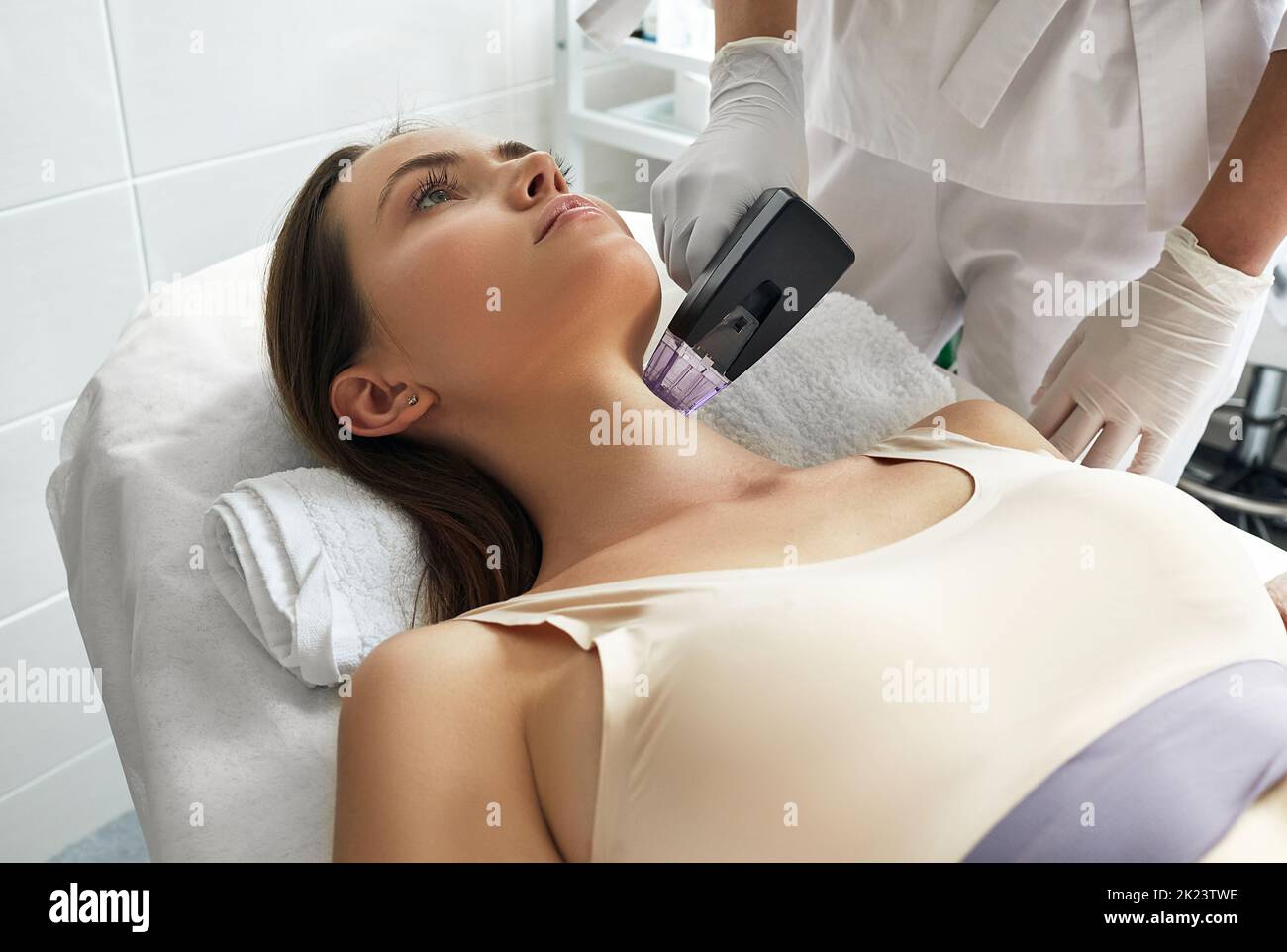 Bella donna gode mentre rf sollevamento procedura per il suo collo e corpo stringendo la pelle con cosmetologist al salone di bellezza Foto Stock