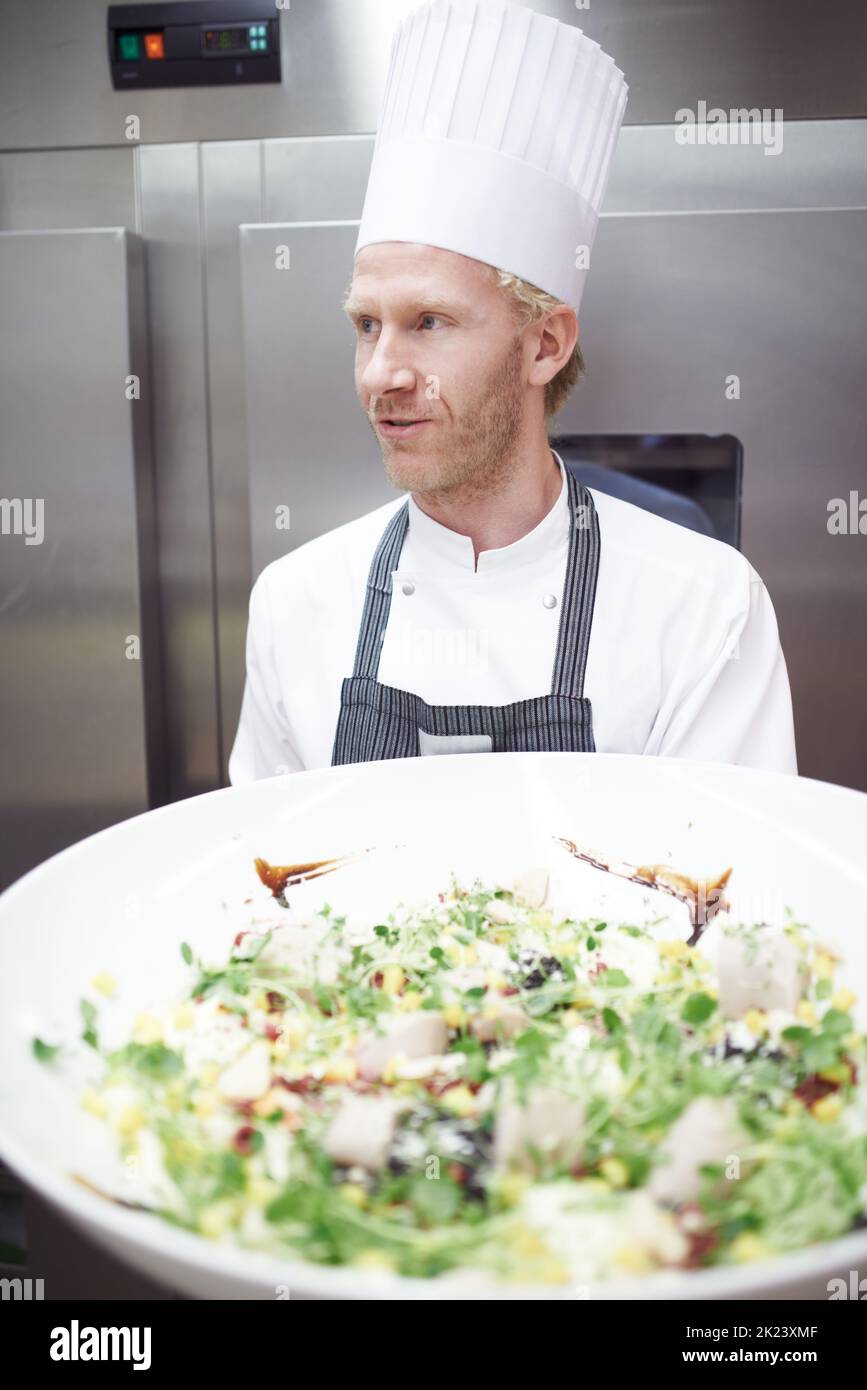 Pronto per il servizio. Uno chef tiene una grande ciotola di insalata in una cucina professionale. Foto Stock