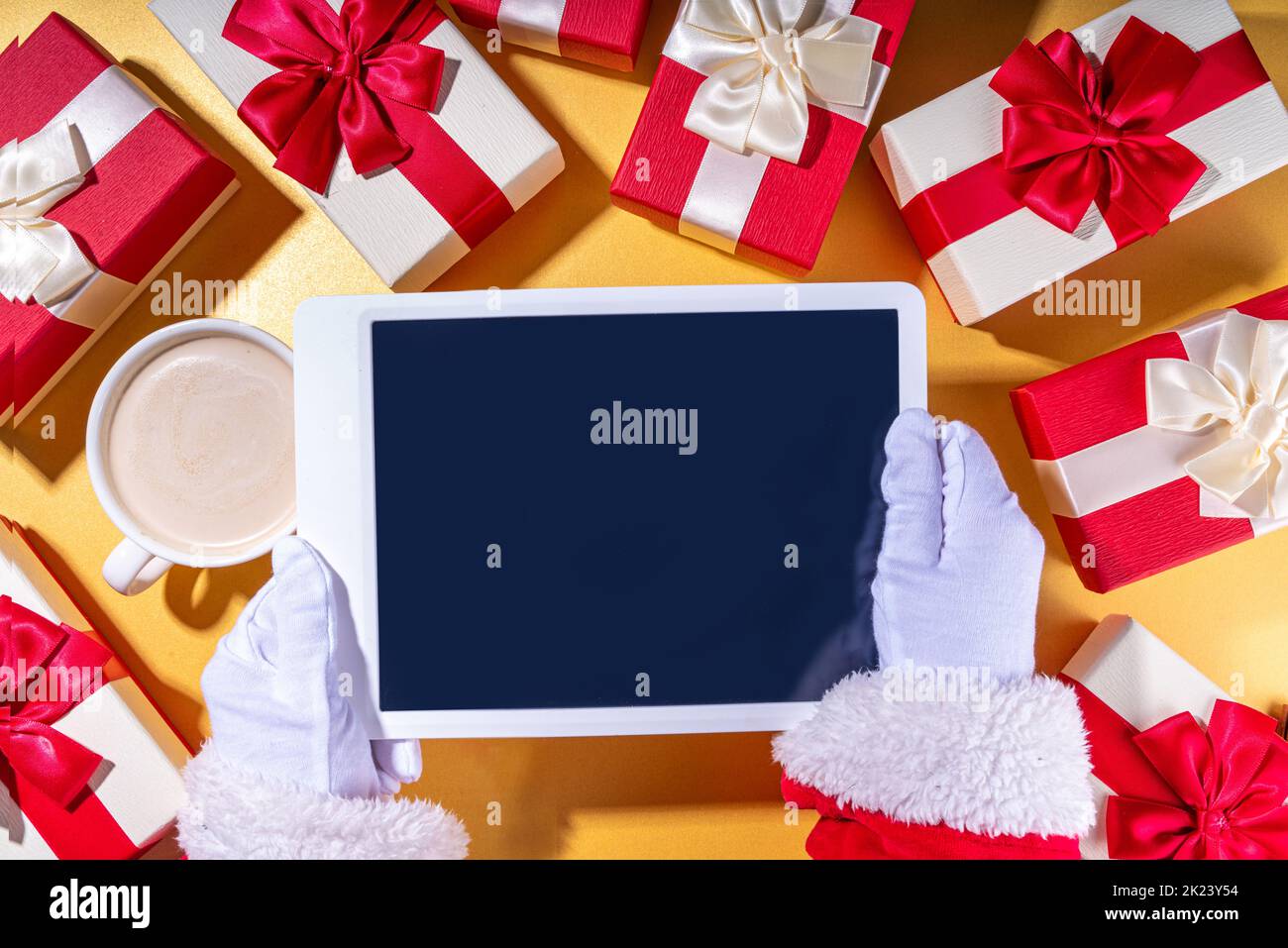 Vendita di Natale, facendo wishlist, regali di preparazione per il concetto di Natale. Mani di Babbo Natale con computer tablet, tazza di latte al cioccolato caldo, confezioni regalo, Foto Stock