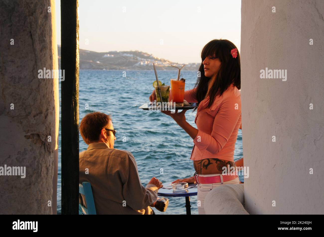 Una cameriera serve bevande esotiche ai turisti seduti in un bar sul lungomare a Mykonos, Grecia Foto Stock