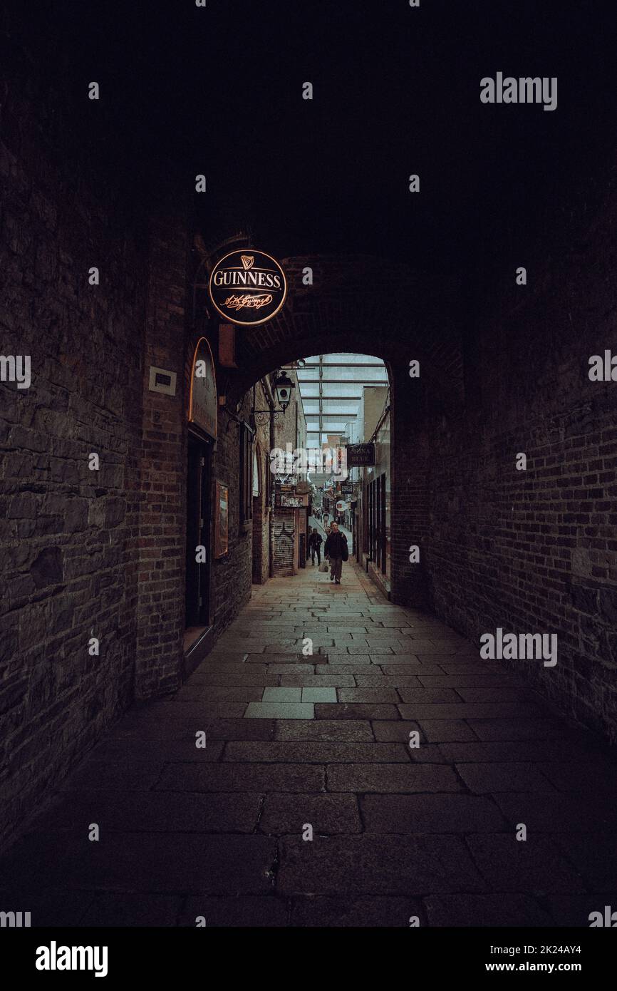 Un vicolo nel centro di Dublino che conduce ad un invitante buco di irrigazione con un iconico logo Guinness su un cartello. Foto Stock