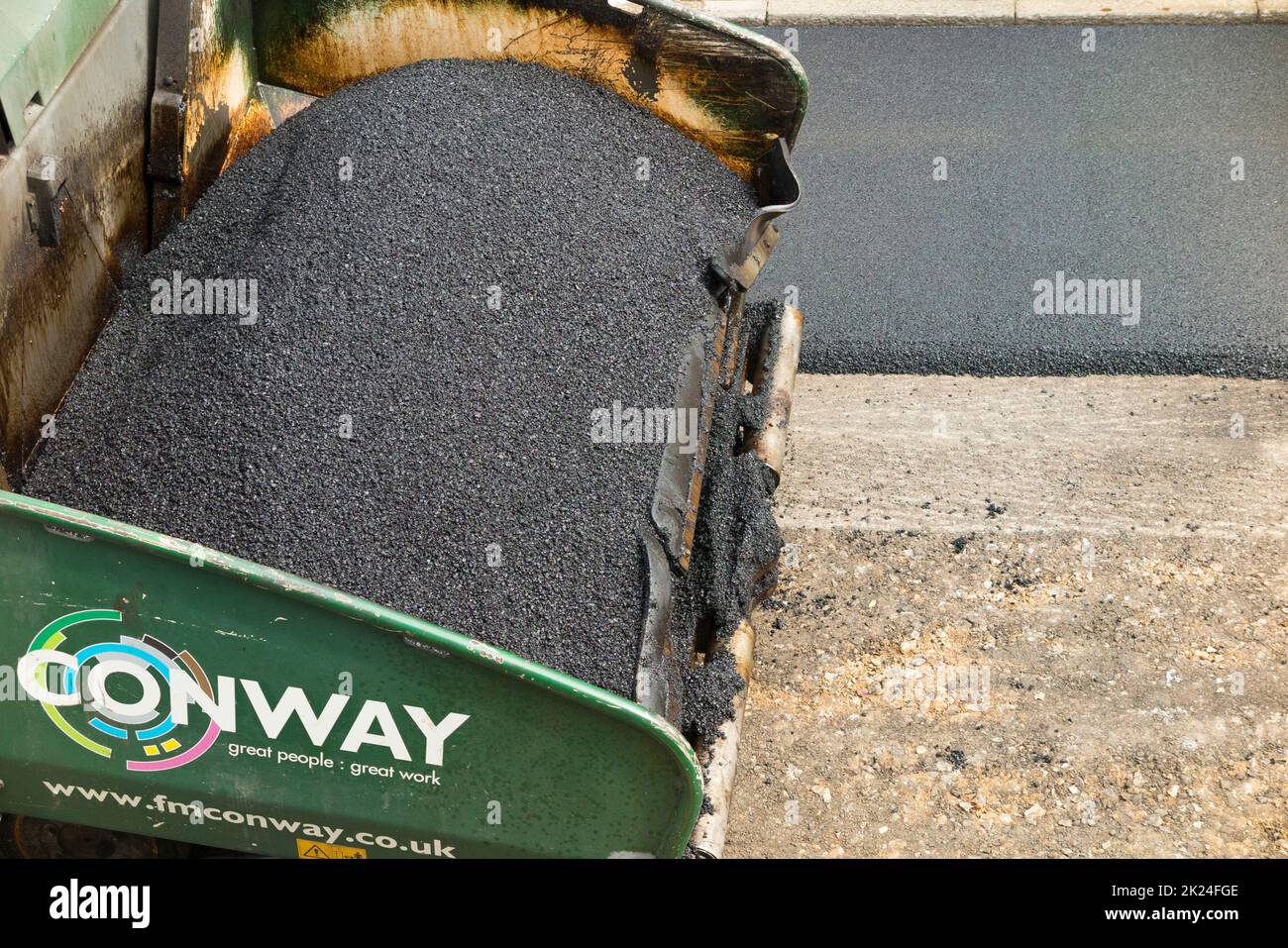 Tarmacadam viene distribuito da una finitrice asfaltata durante il ripavimentamento di una strada residenziale a Twickenham, Greater London, UK. La superficie è stata riaffilata dopo la rimozione della precedente superficie usurata e avvolta. (132) Foto Stock