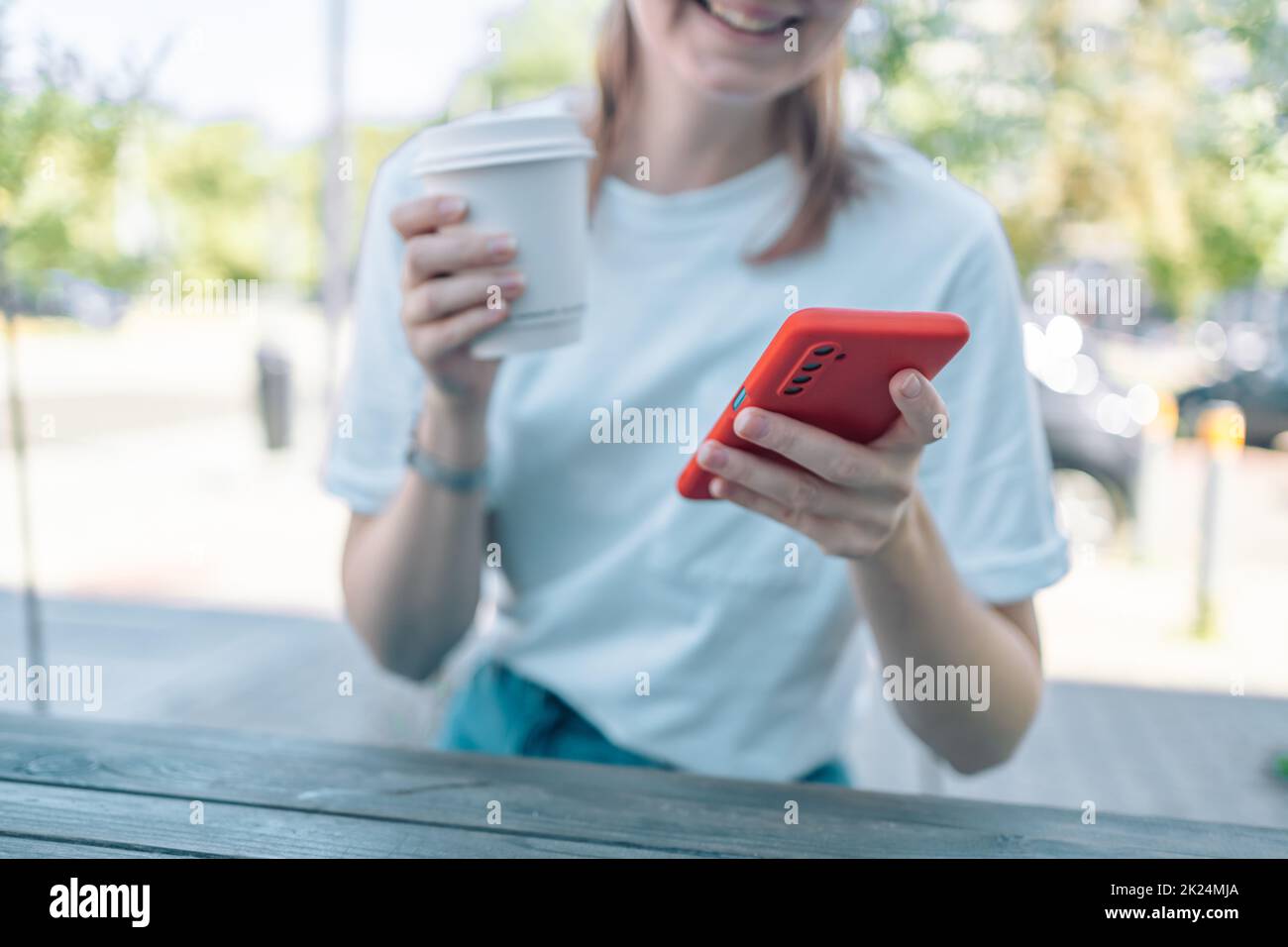 Foto di primo piano tagliata messa a fuoco di una giovane donna caucasica che tiene utilizzando smartphone cellulare per e-banking lavoro remoto, mentre bere caffè in caffetteria Foto Stock