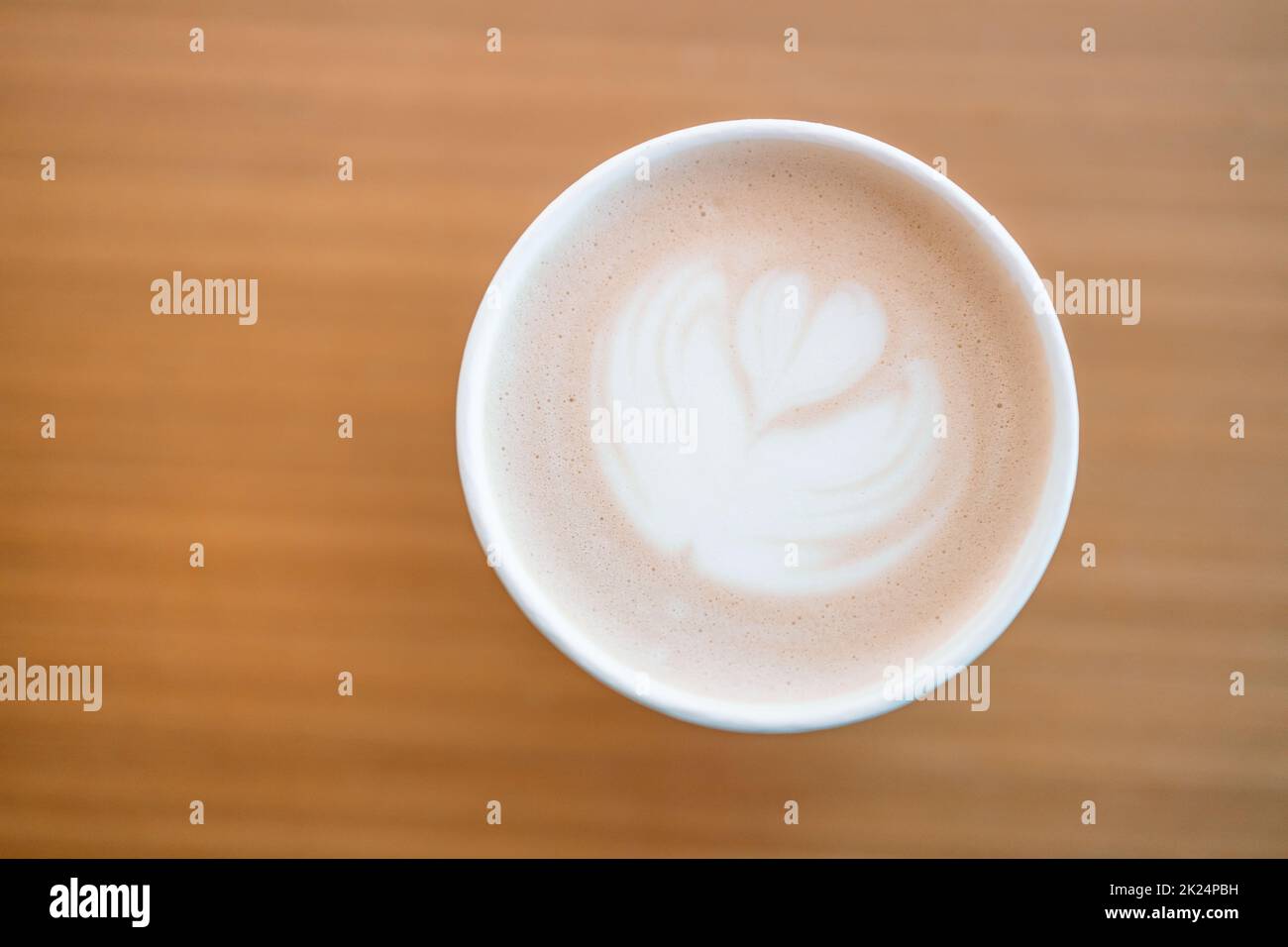 Tazza di carta di caffè cappuccino con latte art sul tavolo di legno nel caffè. Piano di giacitura, vista dall'alto Foto Stock