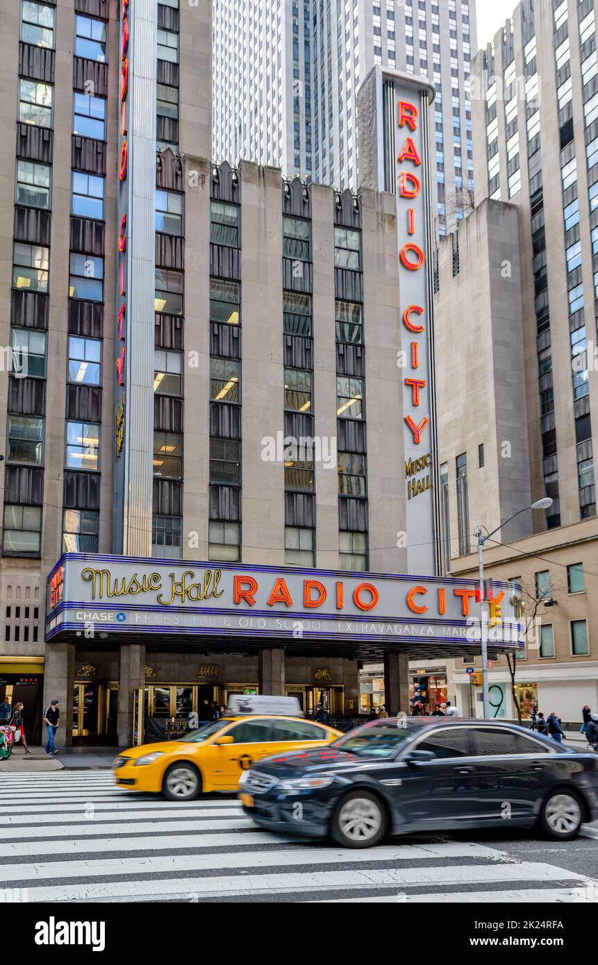 Radio City Music Hall New York City con crosswalk e traffico, un taxi giallo e auto nera in prima linea durante il giorno, verticale Foto Stock