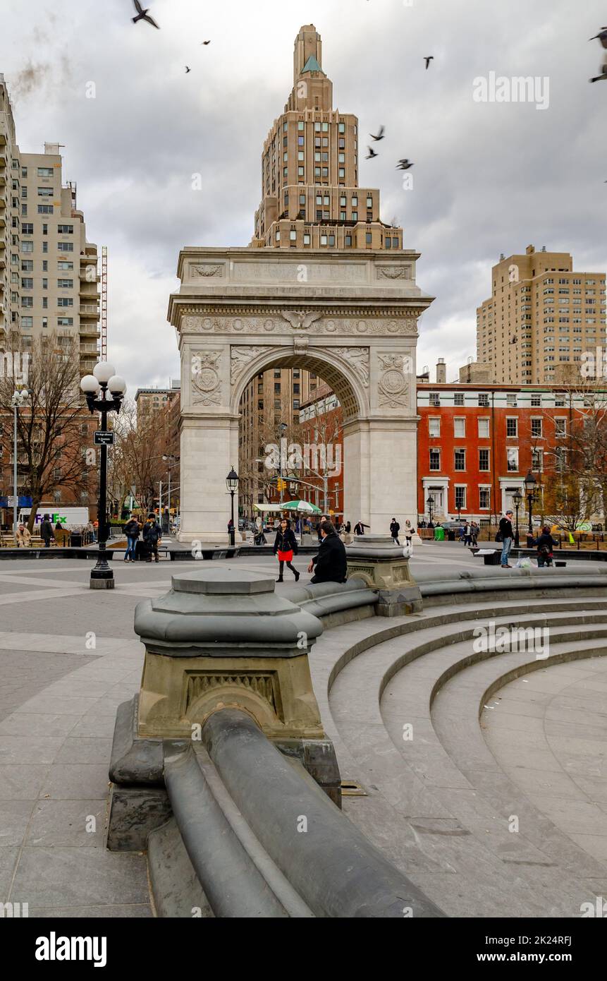 Washington Square Arch, New York City durante una fredda giornata invernale con fontana vuota in prima linea, uccelli che volano sopra l'edificio, persone che camminano in Foto Stock