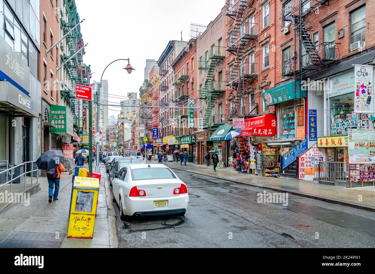 China Town New York City con negozi al dettaglio e persone con ombrello a piedi sul marciapiede, durante la piovosa giornata invernale con overcast, orizzontale Foto Stock