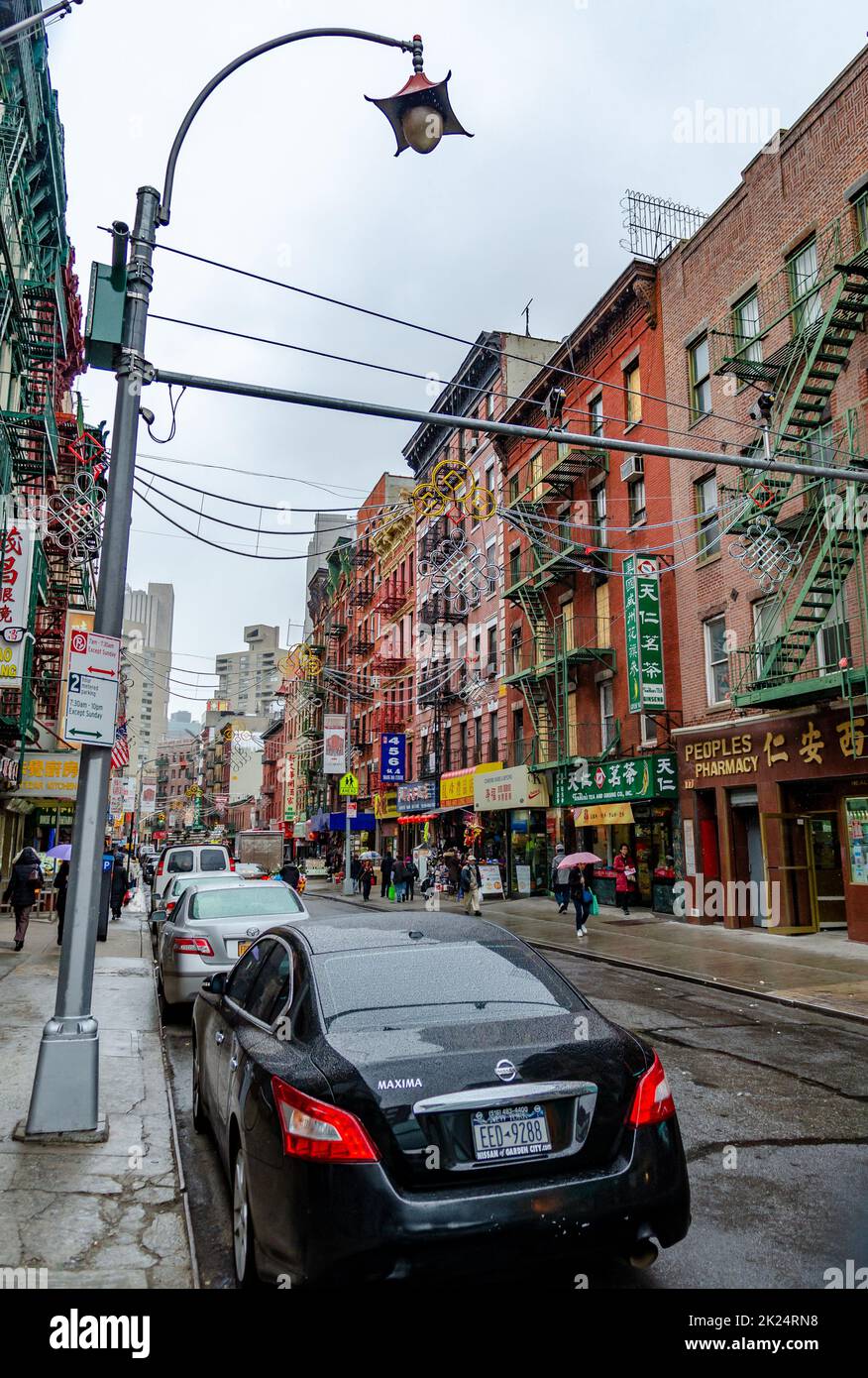 China Town New York City con negozi al dettaglio e persone che camminano sul marciapiede con ombrello, durante la piovosa giornata invernale con overcast, verticale Foto Stock